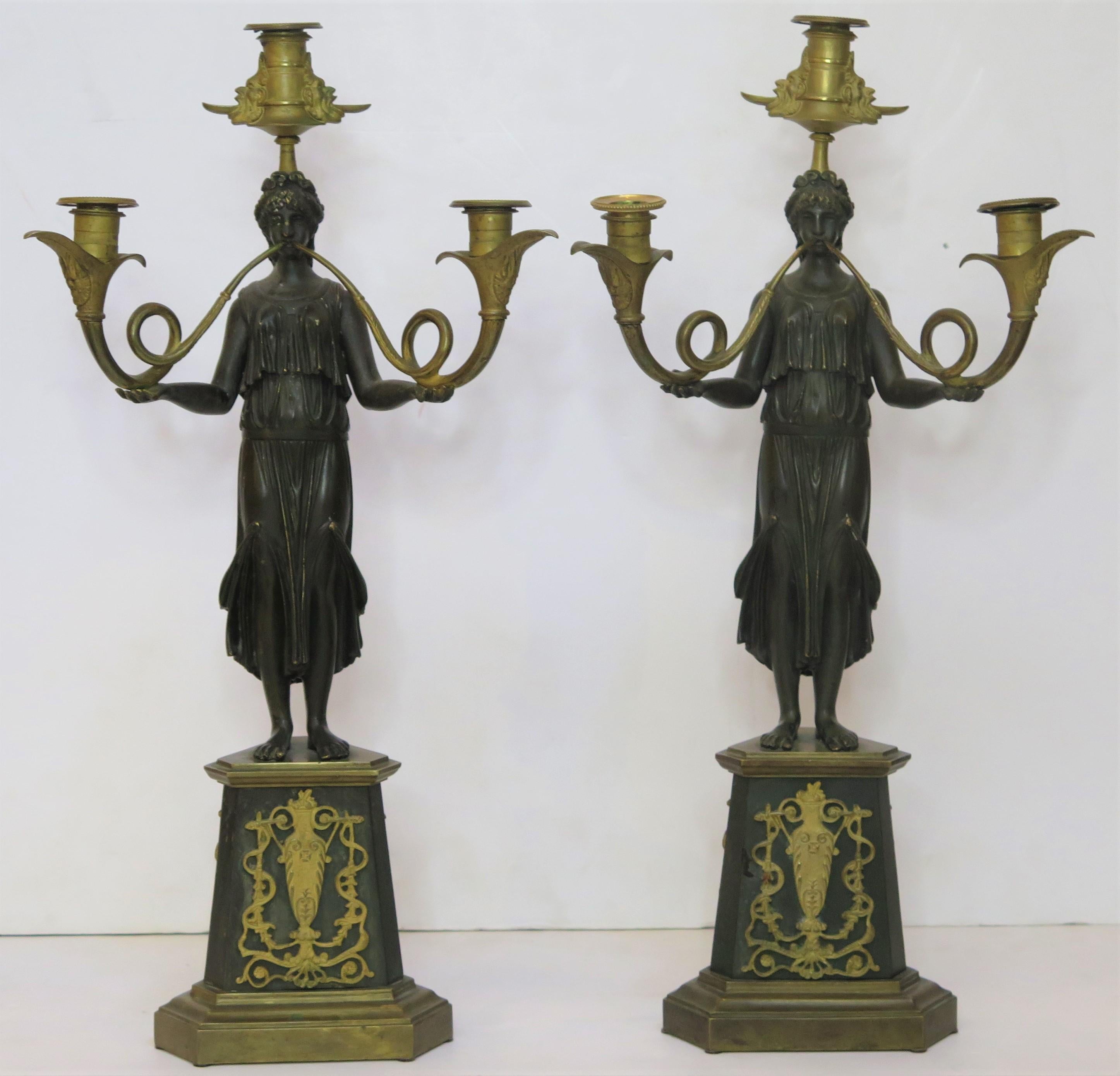 une paire de candélabres en bronze doré et patiné, chacun avec une figure féminine tenant deux couronnes / cornes sur une base triangulaire avec des montures filigranées élaborées, France, 19ème siècle, vers 1830

une figurine présente une fissure