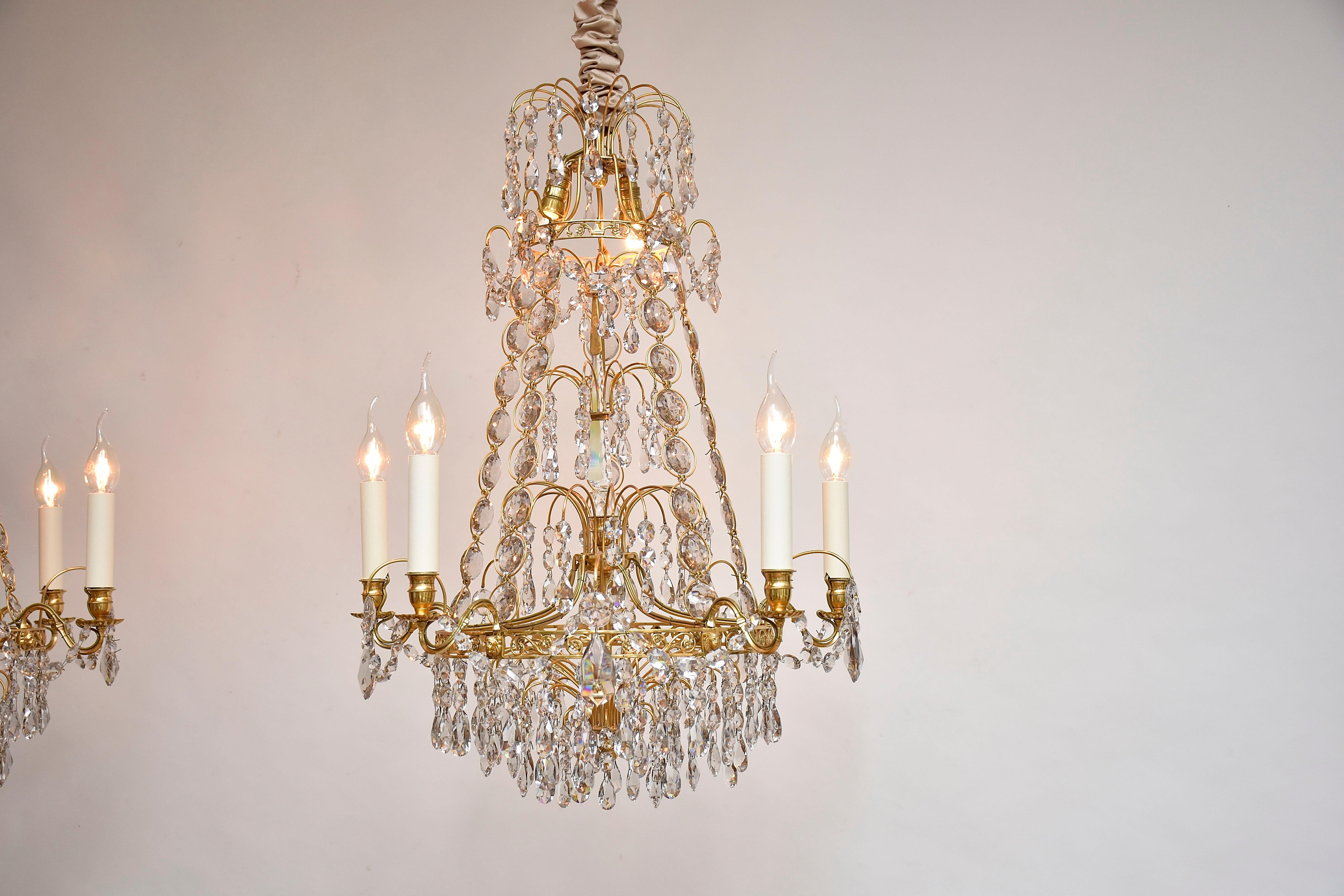 Une élégante paire de lustres de style gustavien.
Chacun avec 7 lumières : 5 lumières autour du lustre et 2 petites lumières à l'intérieur.
Belle qualité en laiton doré.
Décoré de cristaux taillés, de gouttes, de boutons et de chaînes. 
5 chaînes