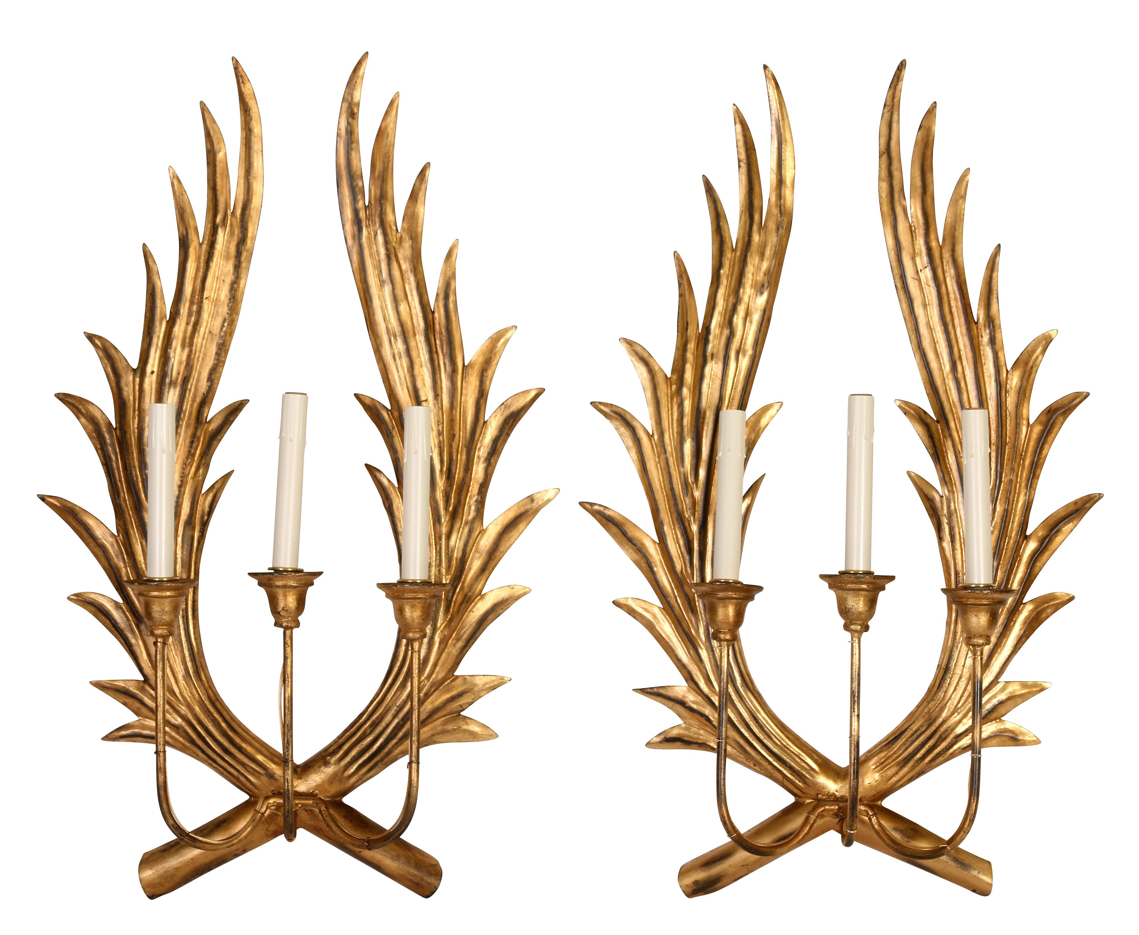 A pair of unusual and striking gilt metal wall sconces with a crossing branches or wings, supporting three arms. A dramatic way to add light to an entrance, dining room or powder room!