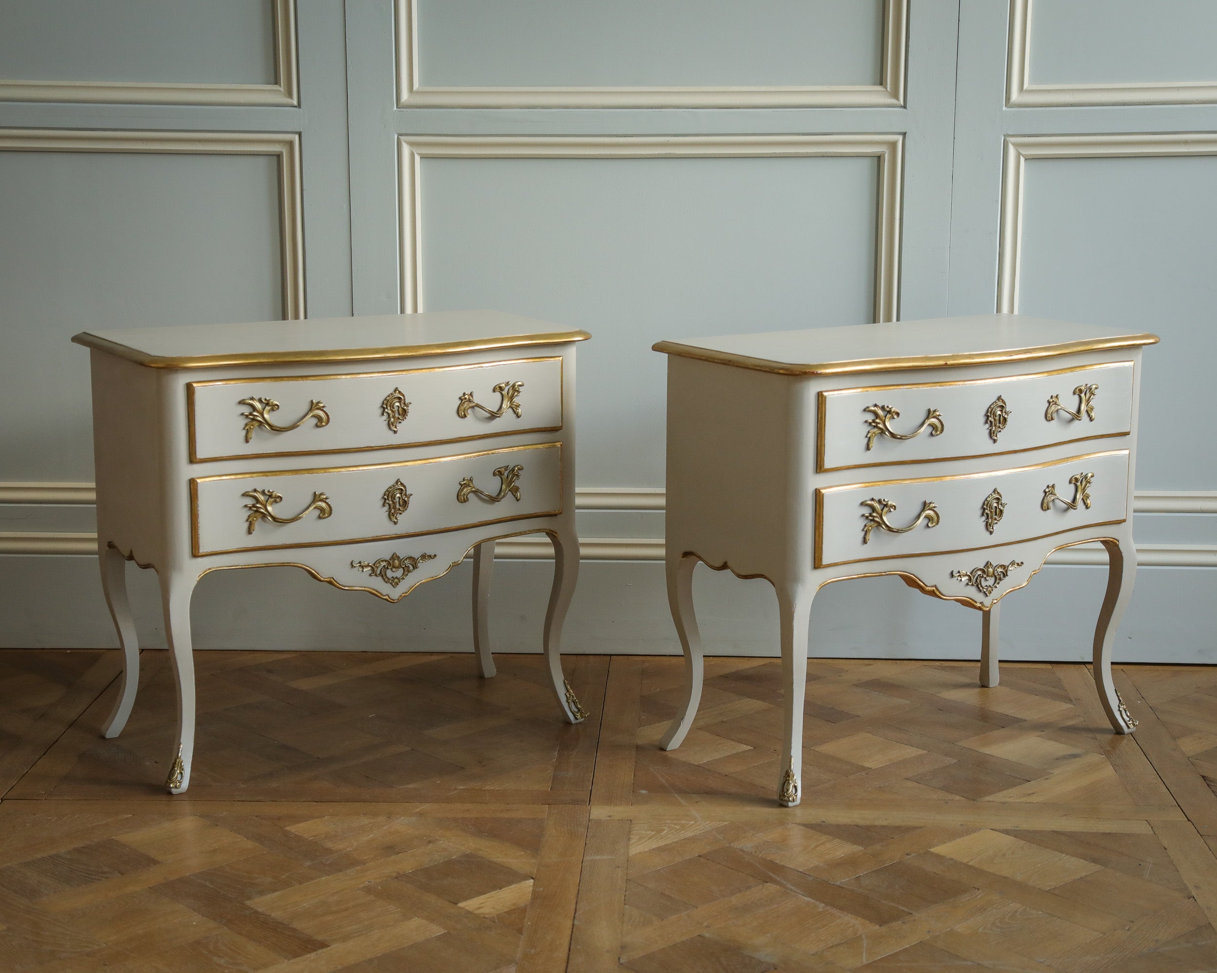 A pair of hand-carved French, Louis XV, style bedside tables/small chest of drawers with a handsome bombe style curved shape. The pieces are hand-finished in a French Blue/Grey with gilded highlights and fitted with antiqued bronze ormolu. Pair in