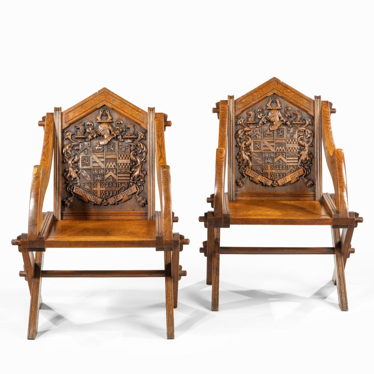 Each of these oak Glastonbury chairs has a pointed back and a fixed rectangular seat. The shaped arms and X-frame legs are attached with protruding pegs, giving the impression of a collapsible or folding chair. The elaborate coats of arms carved