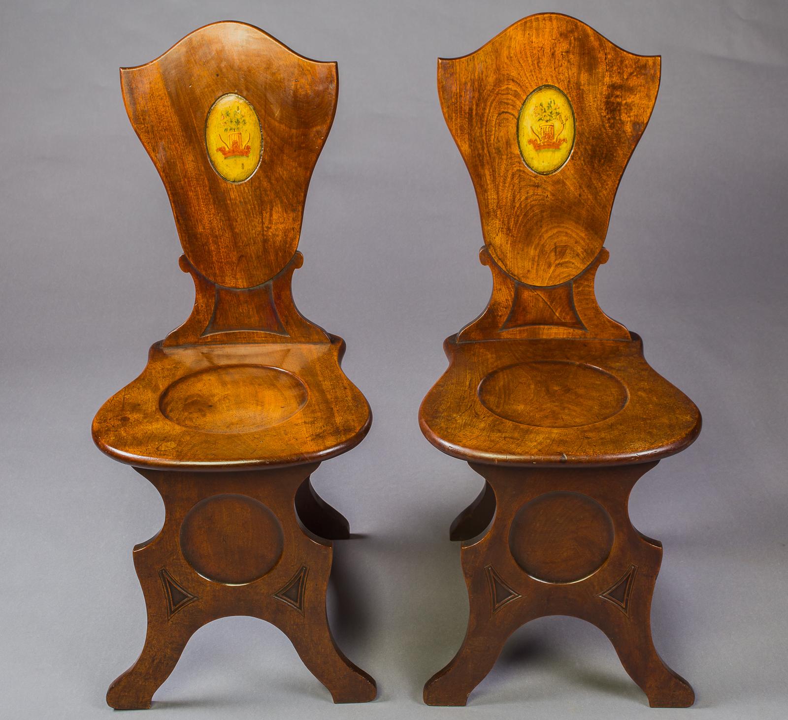 A pair of George III Figured Mahogany hall chairs The shaped solid back with a central oval painted, coat of arms, above an round panel seat,
the colour and patina of these chairs is exceptional.

English, Circa 1750
Measures: Height: 38inches,