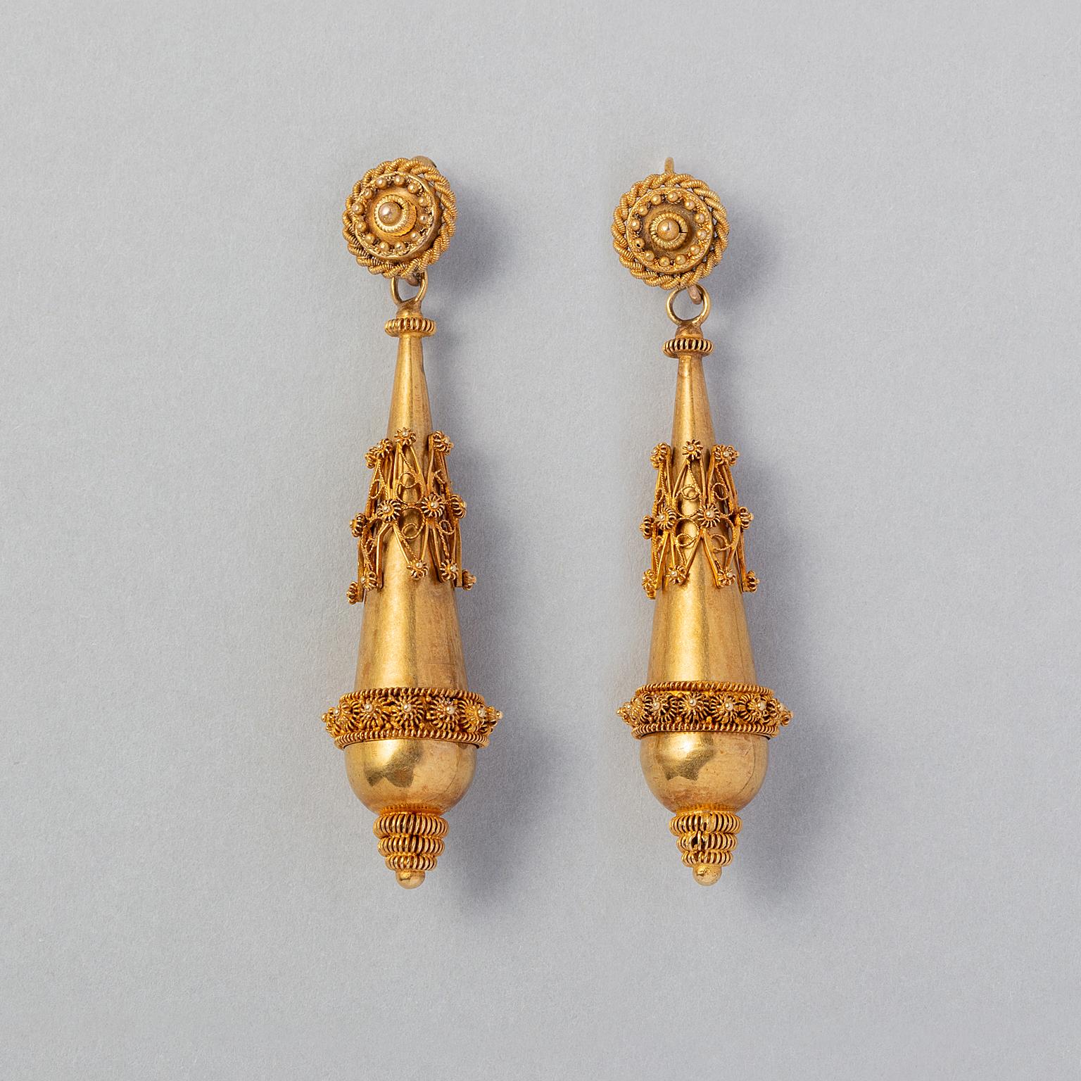 A pair of 15 carat yellow gold torpedo earrings with long dropshaped, hollow gold pendants with a seprate loose gold band around the middle with detailed filigrain. Above and at the bottom are more filigrain decorations. On the top is a round 