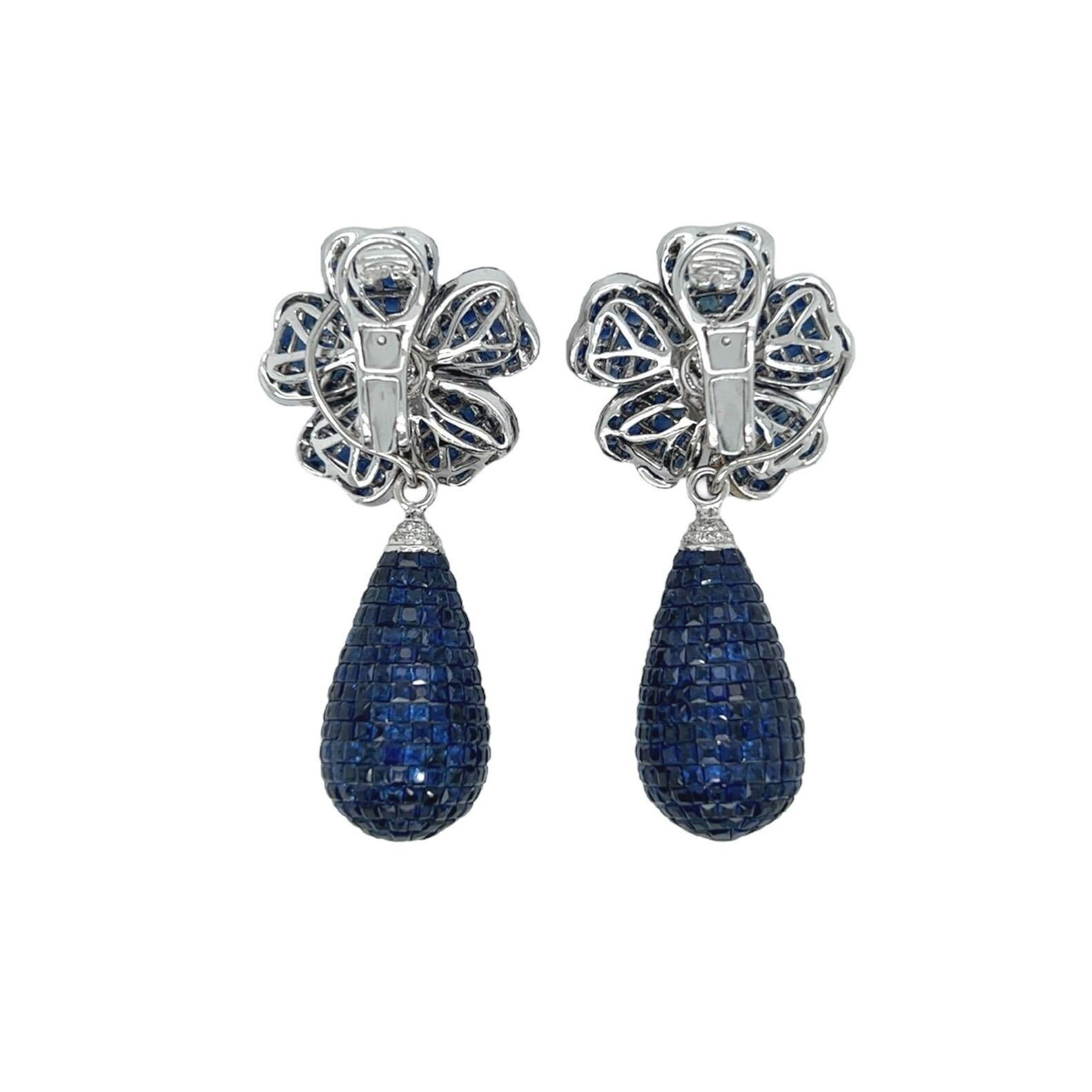Ein Paar Ohrringe aus 18 Karat Gold mit Saphiren und Diamanten.  Jeder Ohrring hat die Form einer Blume mit fünf unsichtbar gefassten Saphirblättern im Kaliberschliff, in deren Mitte sieben  runde Diamanten im Brillantschliff, die an einem