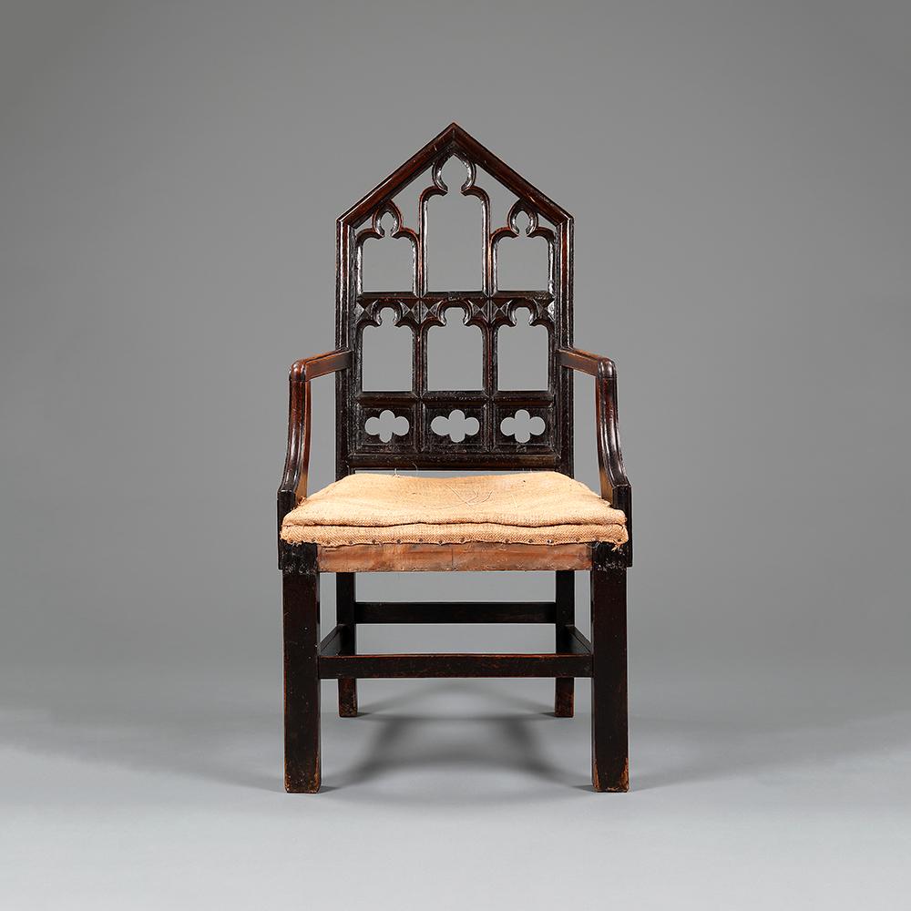 A pair of oak Gothic hall chairs, the triangular arched back rests with carved trefoil and quatrefoil tracery, the squared legs joined by stretchers, and with down swept arm supports.