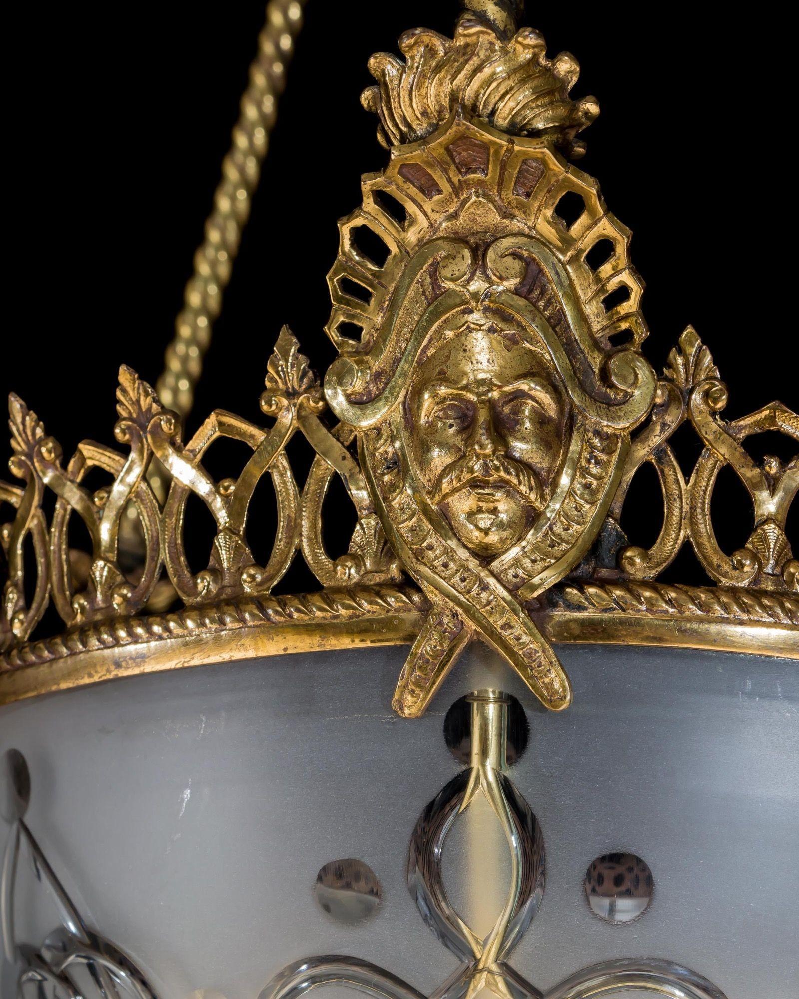 The gilt lacquered metalwork suspended upon rope twist rods, supporting a fretted motif band fitted with applied masks, this mounting a frosted glass bowl cut with gothic decoration.