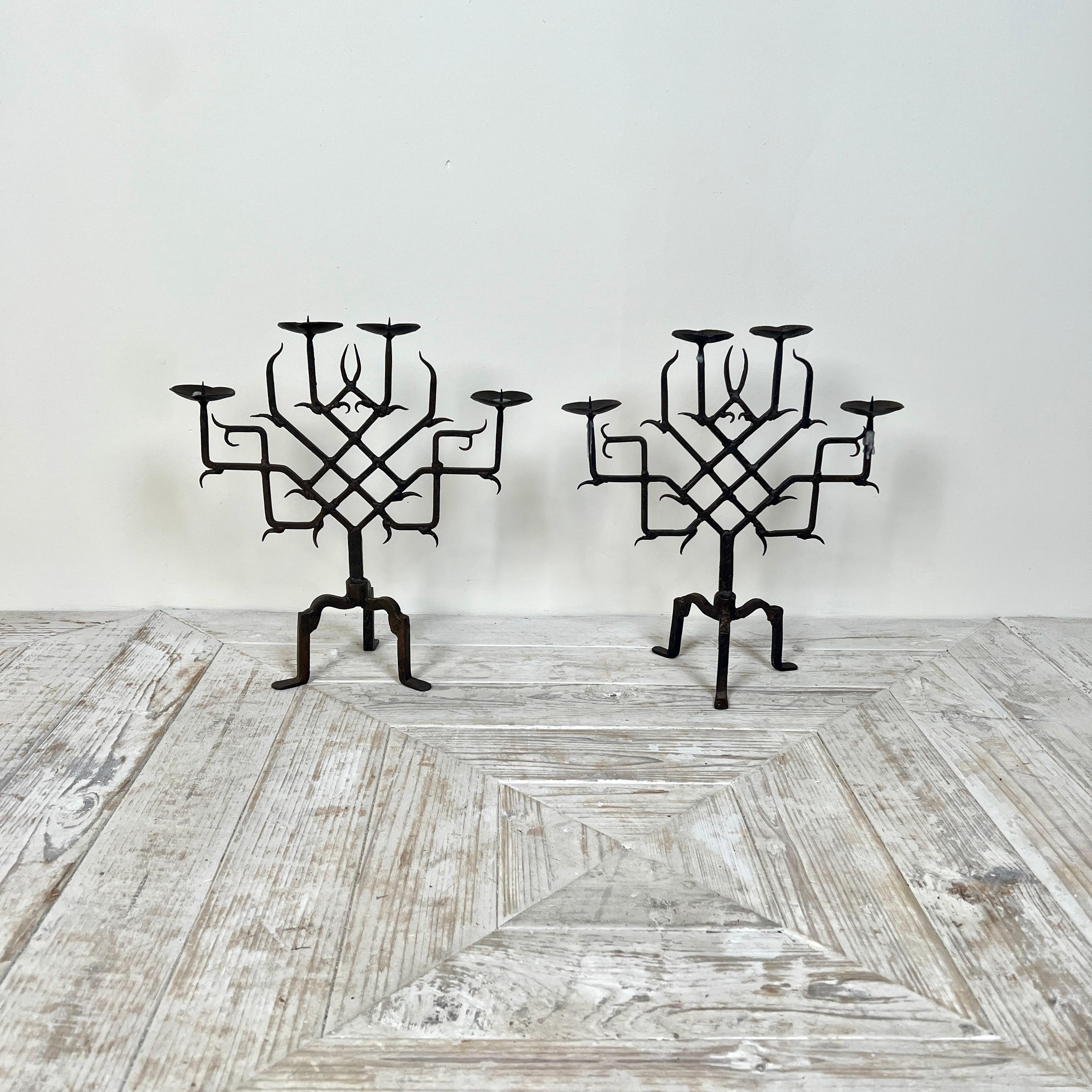 Coppia di candelabri in ferro battuto in stile gotico. Le quattro teste delle appliques sono sostenute da una cornice a reticolo simmetrica con decorazioni a forma di artiglio. Il tutto poggia su gambe a tripode che terminano con piccoli piedi.