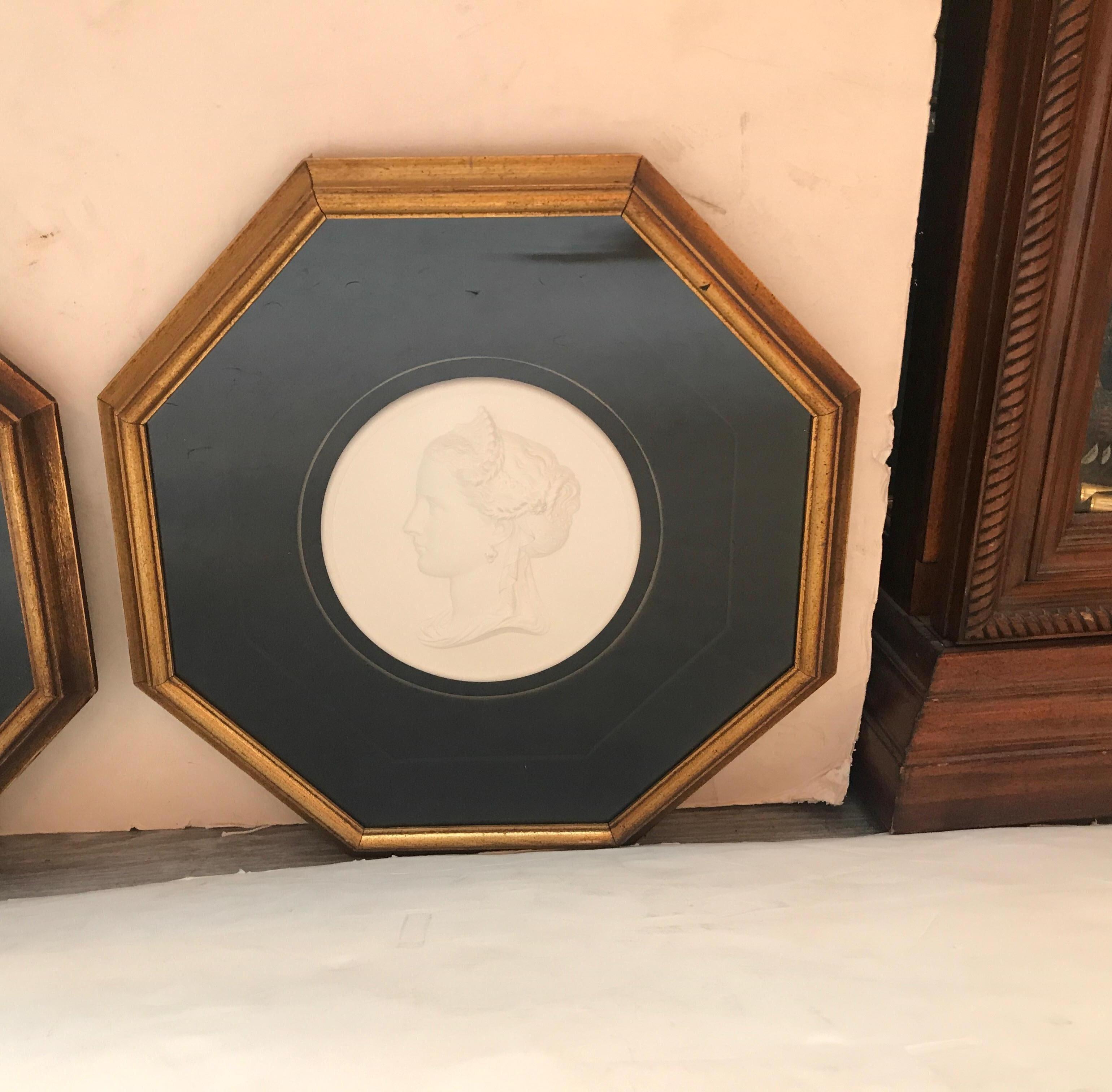 A mirror image pair of bas relief giltwood framed plaster plaques depicting neoclassical profile portraits on a black velvet background. Each one of a beautiful neoclassic style young woman with crown and aristocratic clothing.