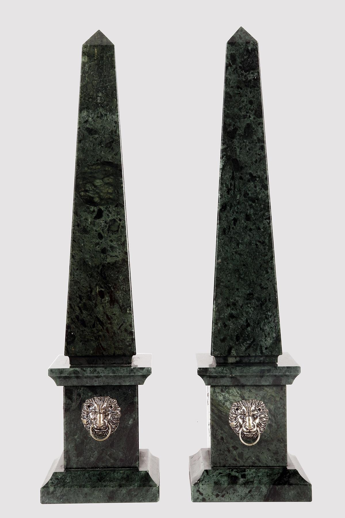 A pair of Grand Tour obelisks. Made of Green Alps marble. On the front side of the plinth, there is a bezel with a silver mask depicting the head of a lion. Italy second half of the 19th century.