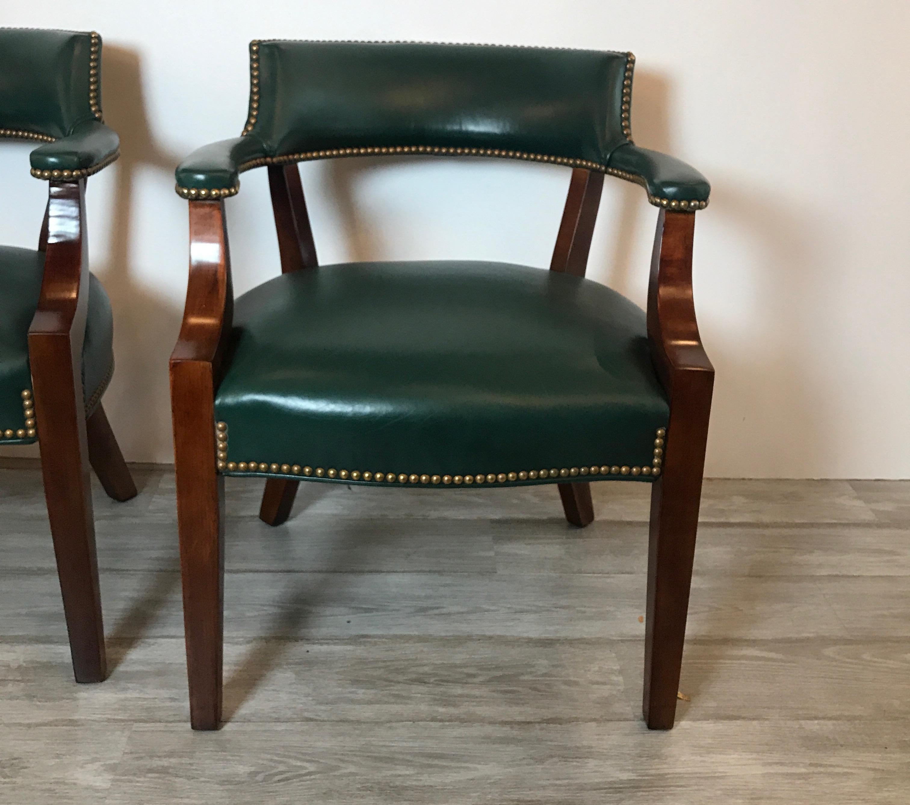 Classic pair of leather library chairs with nail head trim and mahogany frames. The comfortable rounded backs with attached arms with leather seats. Excellent well cared for vintage condition.