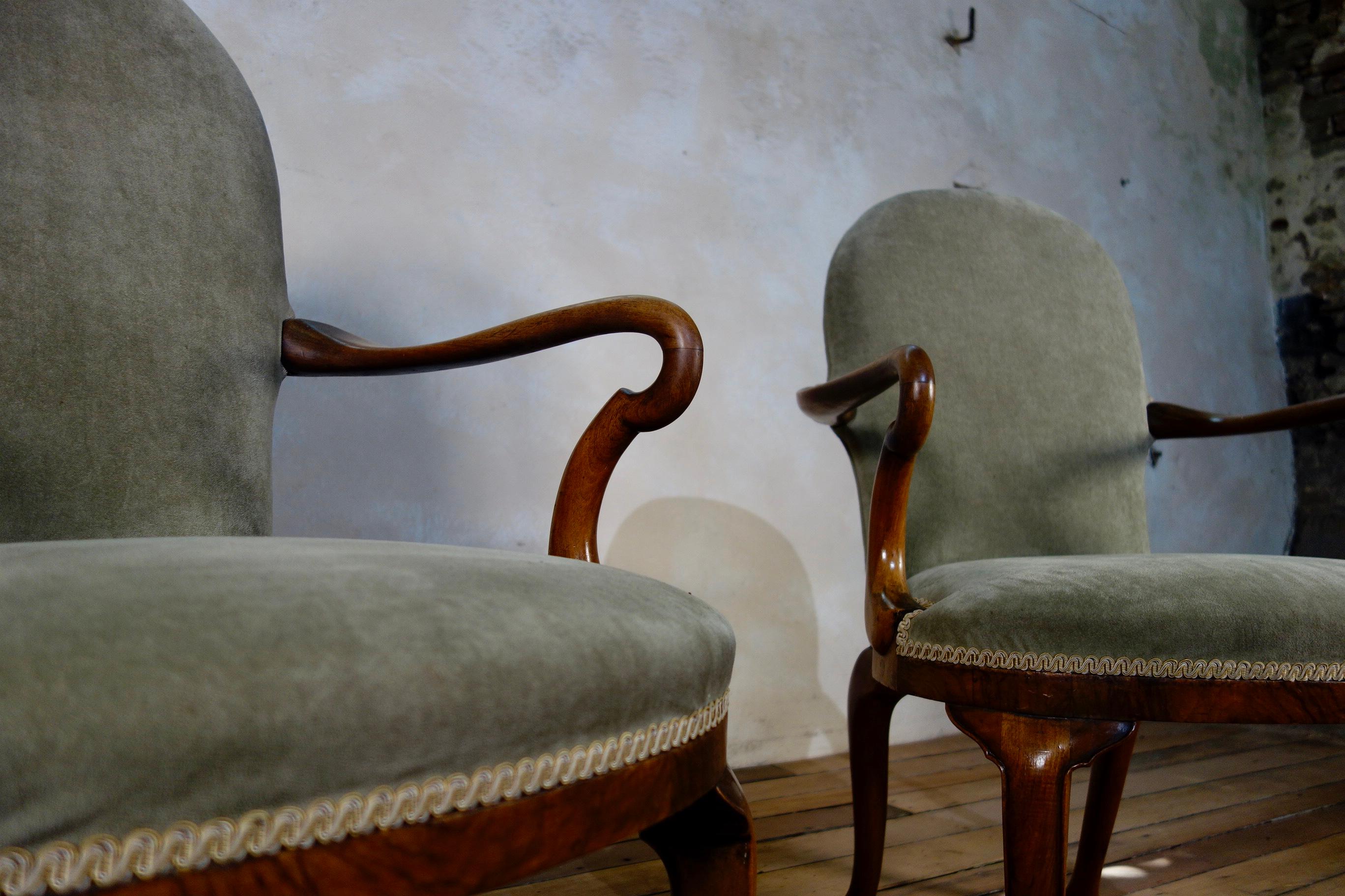 A pair of George I style armchairs, featuring walnut shepherd crook arms and rounded upholstered back. Raised on raking rear legs with front cabriole legs - sat on pad feet. This is one pair from a set of three pairs of identical chairs, with each