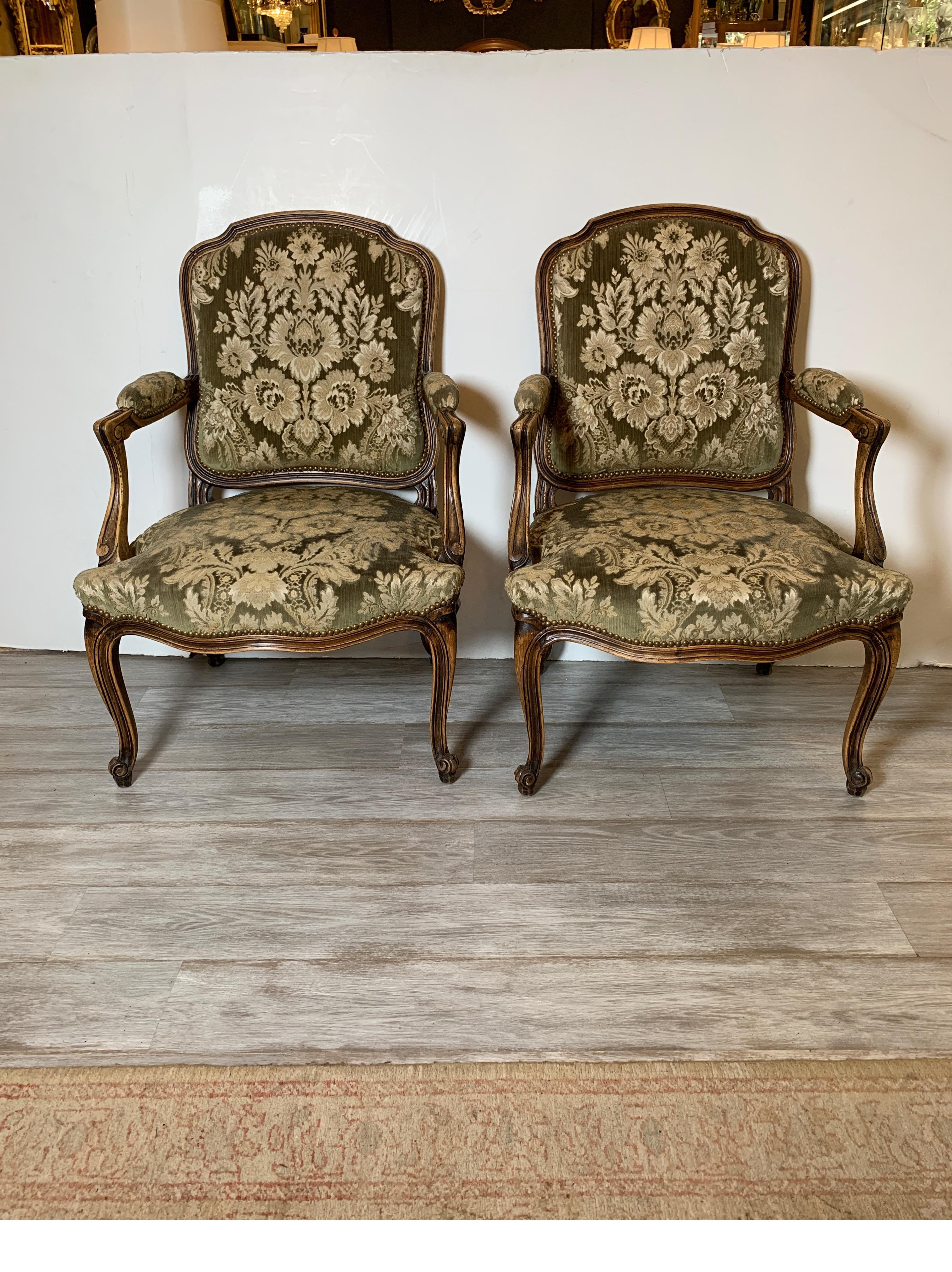 Ein Paar französische geschnitzte Fauteuils-Stühle mit italienischem Samtdamastbezug. Der salbeigrüne Samt mit zartem Golddamast ist mit Messingnägeln verziert. Der Holzrahmen hat eine natürliche, abgenutzte Oberfläche. Die Sitze sind mit einer