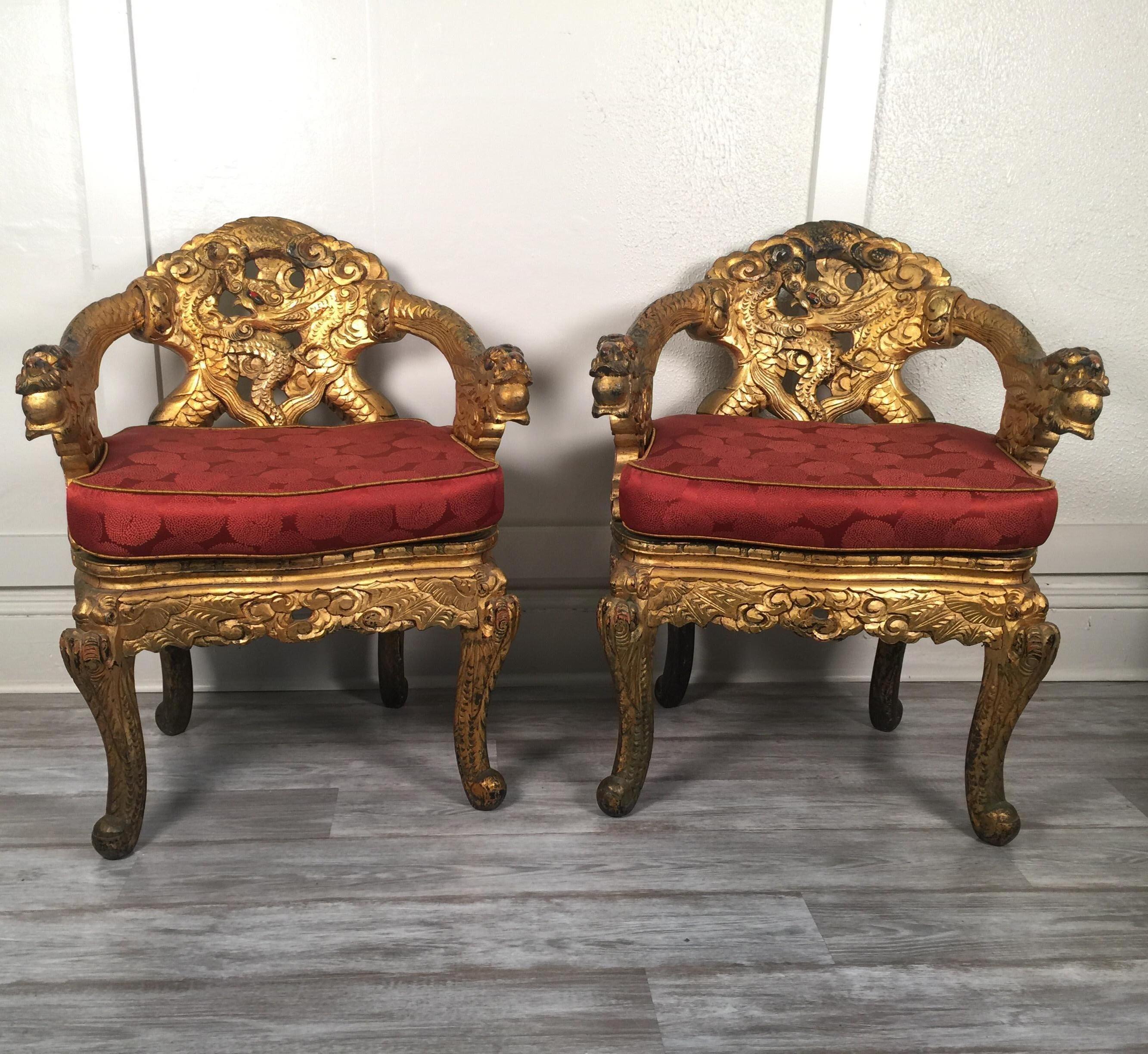 A pair of early 20th century Japanese caved armchairs with custom silk cushions. The chairs with carved dragons along the curved backs and curved legs are in a Chinese style from a much earlier period. The surface with gold wear showing the black