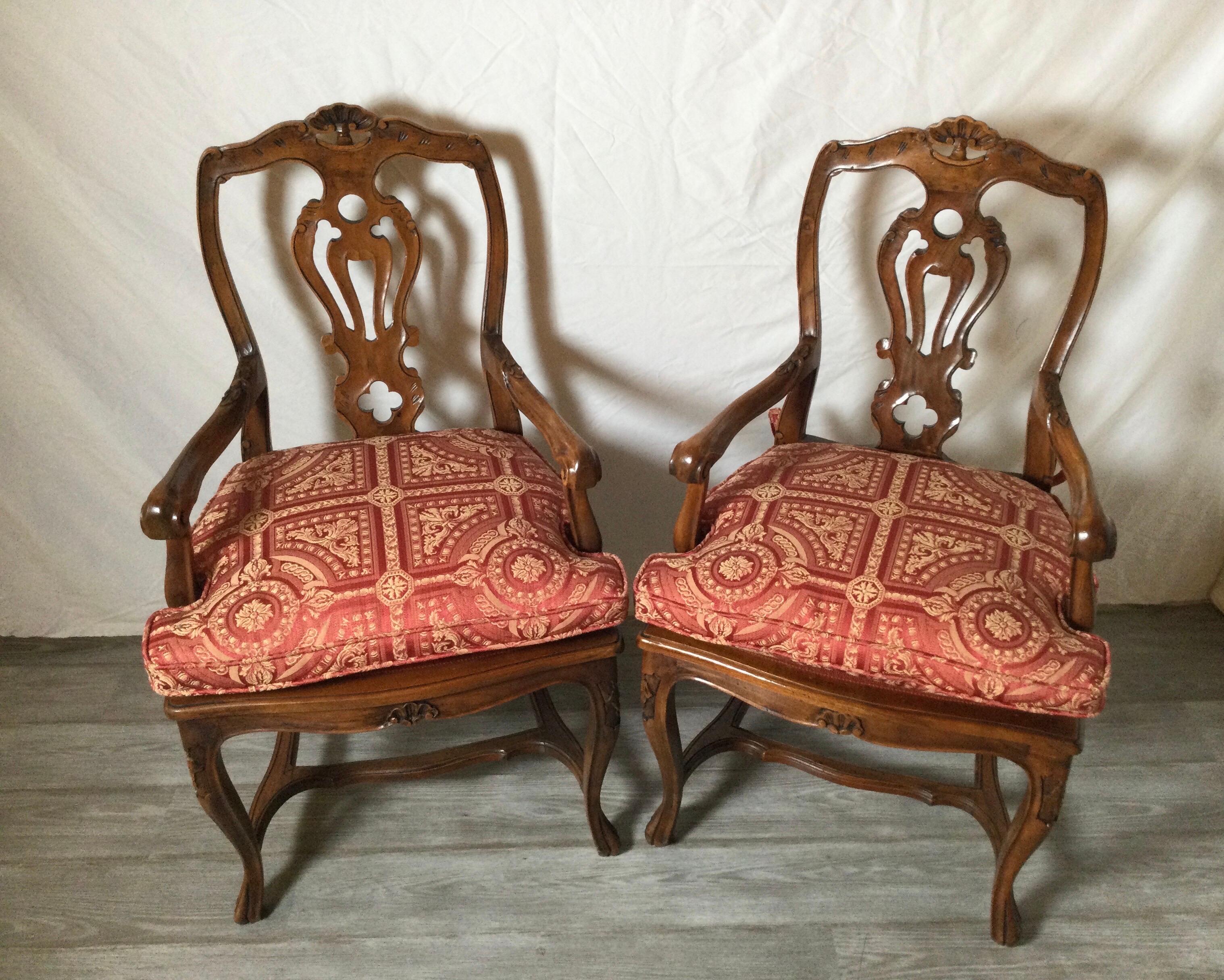 A beautiful pair of hand carved walnut chairs with new custom seat cushions. The shapely backs with open splats and open hand carved arms. The bases with a well crafted stretcher supporting gently curved legs in the French taste but made in Italy