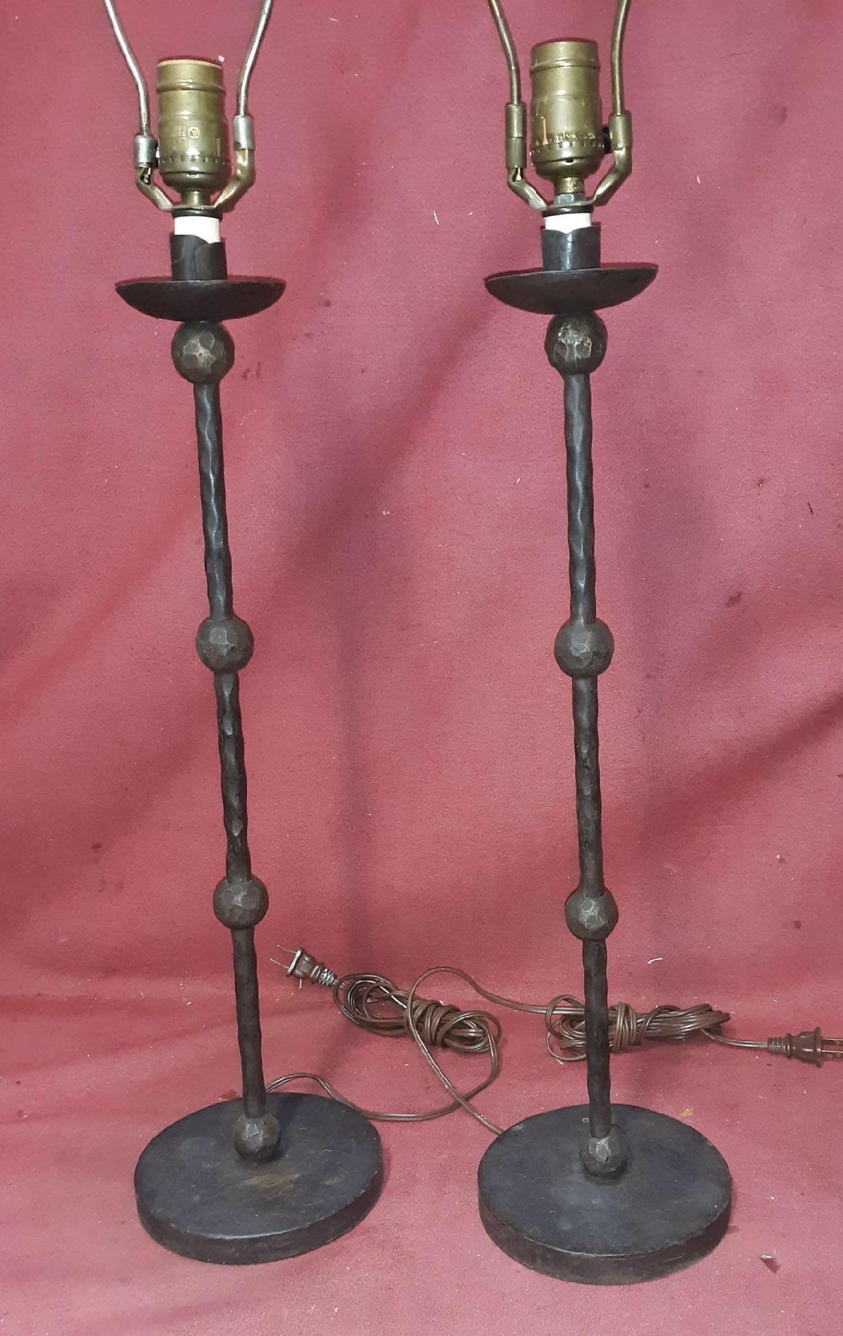 A pair of 1970's forged and cast iron tall candlestick lamps in the manner of Alberto Giacometti. The central pole with twisted sections with multi-faceted balls with round bases. A total of 30 inches to the top of the harp. 21.5 inches to the top