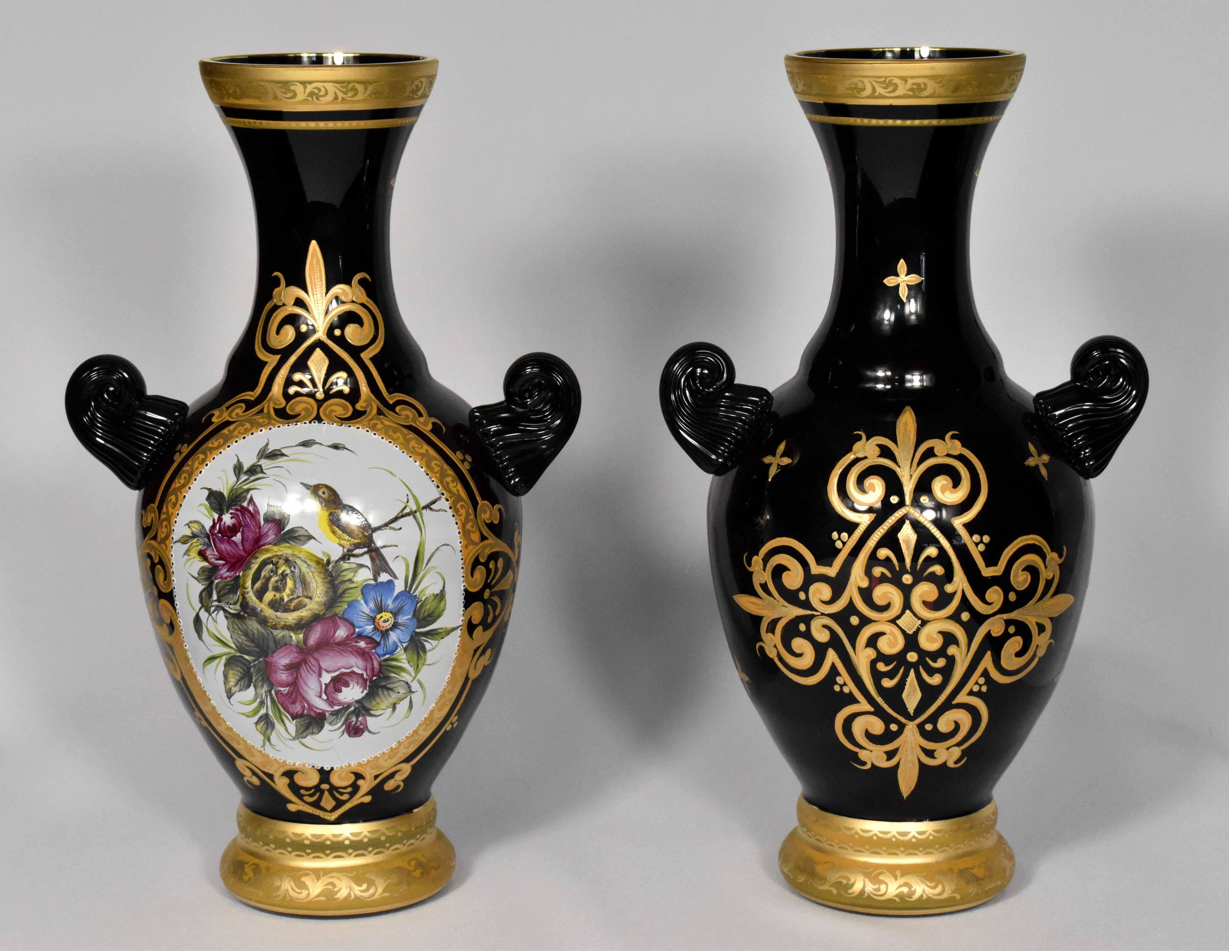 This beautiful pair of vases is made from black/purple glass. 
They’re hand-blown in a glass atelier in the Nothern Czech Republic using traditional techniques from glass masters of the 19th century.
They are decorated with ornamental paintings of