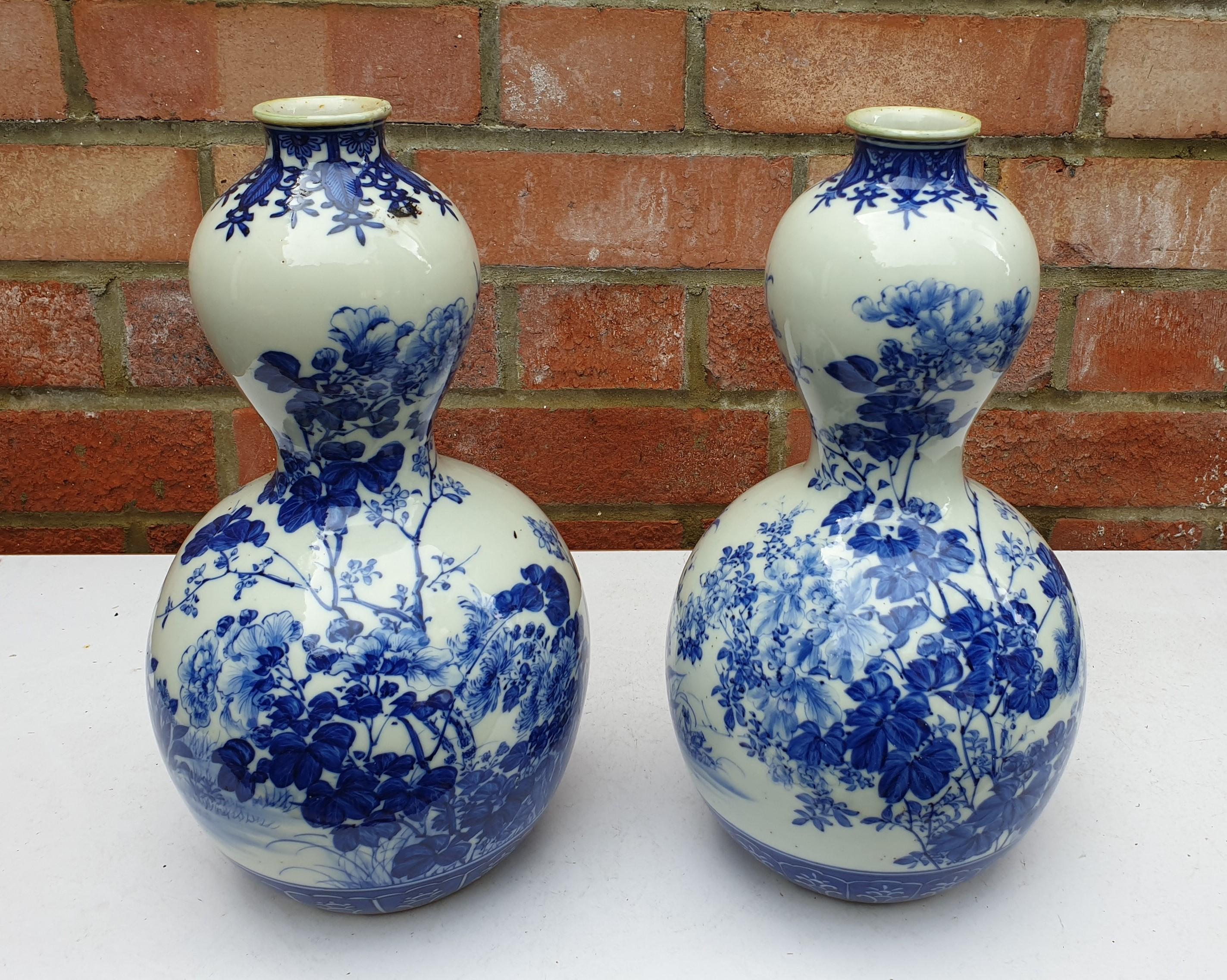 Pair of Japaneses hand painted blue and white double gourde vases. Produced in the Meiji Period, with floral scenery dressing the vases. The vases are bulbous in shape with a small slender waist. Throughout the vases scenery of trailing branches and