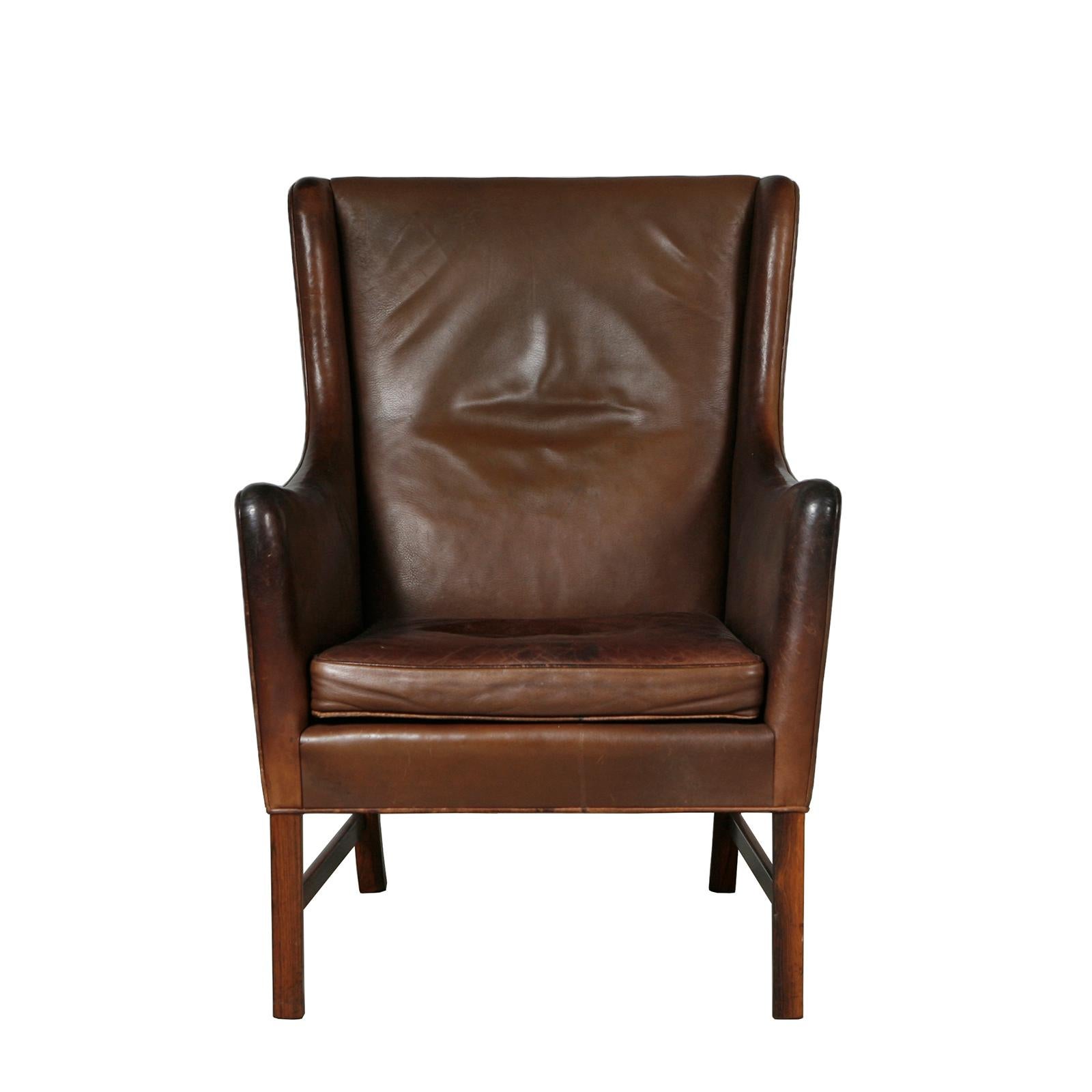 This pair of elegant high-back lounge chairs retain the original deep brown leather which is in excellent condition and has a beautiful patina. The bases are made of Brazilian rosewood. Designed by Ole Wanscher in 1960 and exeuted by master
