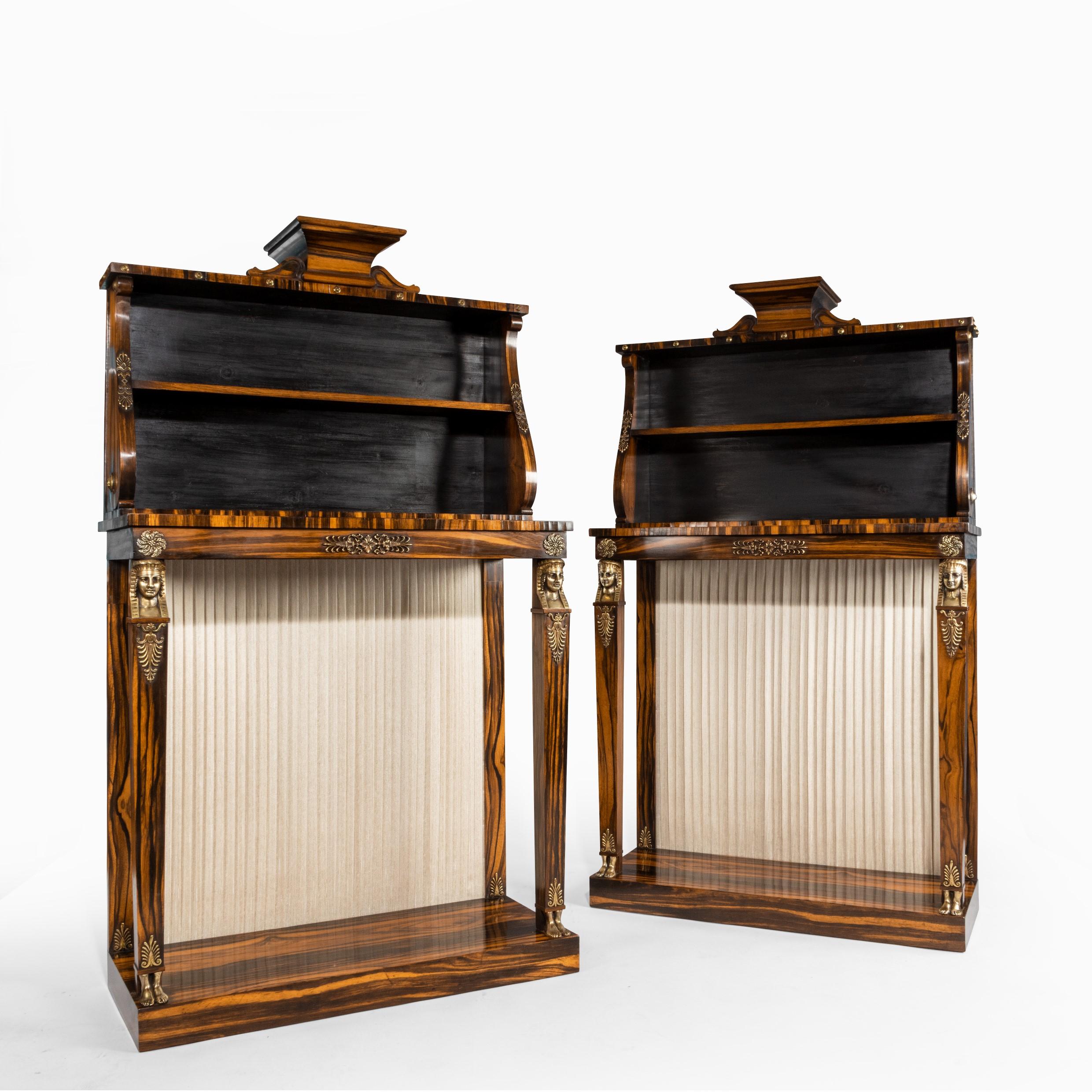 A pair of high Regency Coromandel and ormolu bookcase console tables in the style of Thomas Hope, each of rectangular form with two square section pillars in the form of pharaonic terms with bare feet, on a solid plinth, surmounted by two shelves