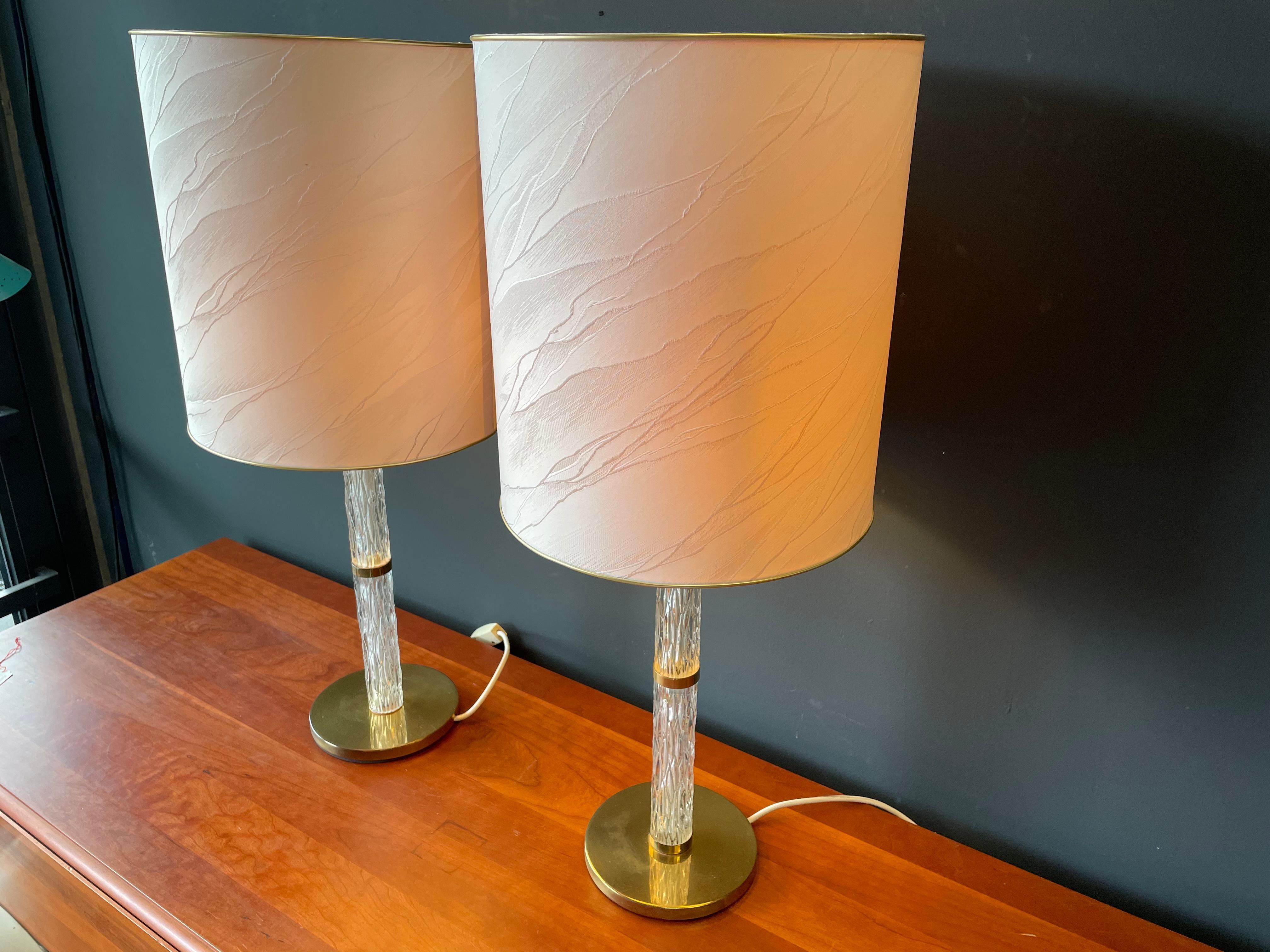 Hollywood Regency table lamps by Kaiser with ice glass base.
The lamps are from the years around 1965 to 1970. The special feature of this pair of lamps and typical of this period are their lamp bases. These are textured glass with polished brass