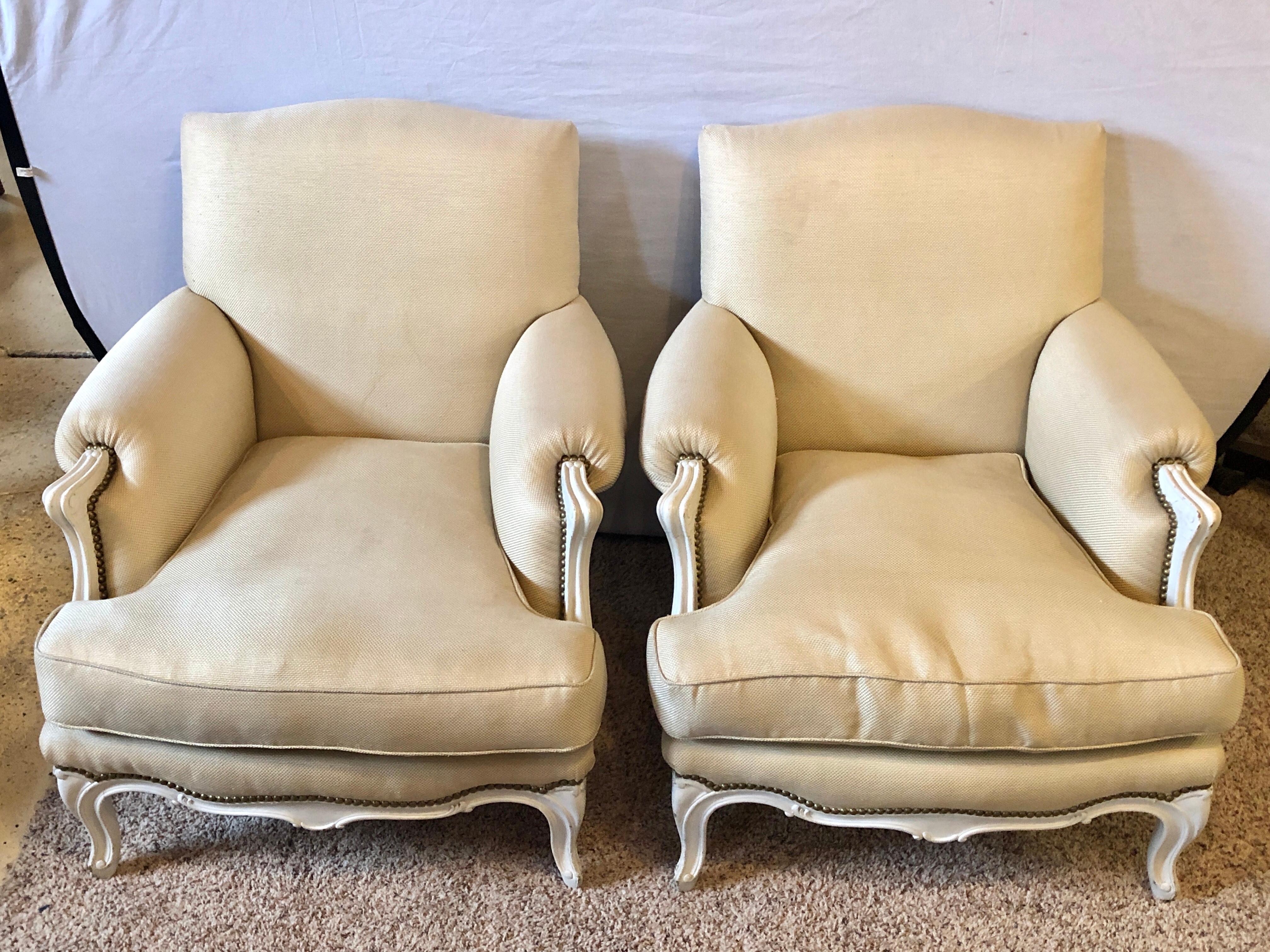 A pair of Hollywood Regency Louis XV style linen covered bergere / armchairs each having comfortable down cushions. The pair having paint decorated frames in a lovely fabric that is fully tacked on all sides and the back.