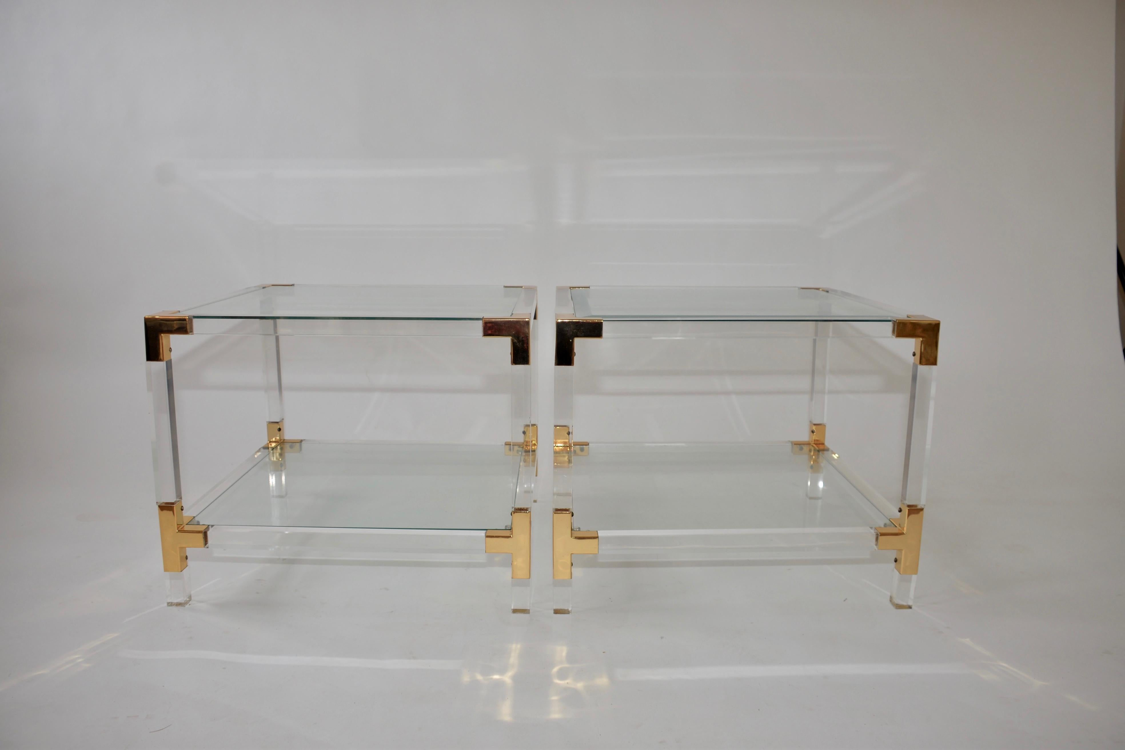 A pair of Lucite and glass Hollywood Regency side tables. The frames are Lucite with two glass shelves and the top shelf is beveled glass. Each corner is finished in brass plating.