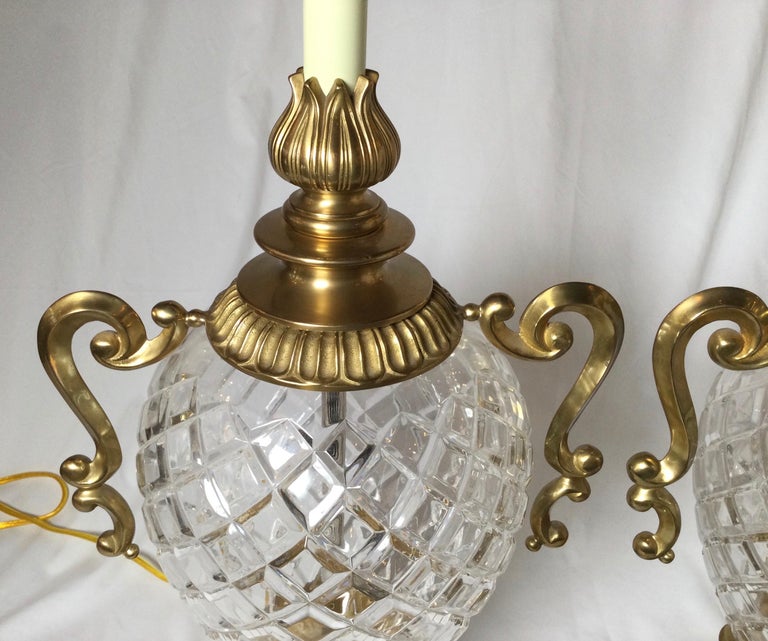 A pair of good quality crystal and brass pineapple motif bulbous lamps. The diamond crystal bodies with brass tops and bases with cast brass scrolled handles. Shades are for photographic purposes only and not included with the lamps.