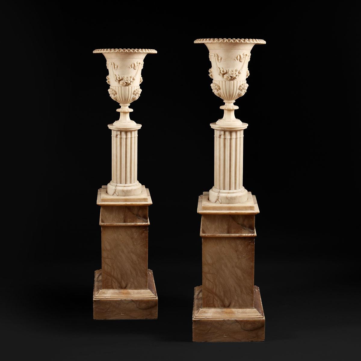 Floor standing classically carved alabaster vases on fluted columns and square stepped pedestals Carved with Satyre masks and foliate swags suspended from ribbons. Electrified and Illuminated throughout, including the base, the column, and the