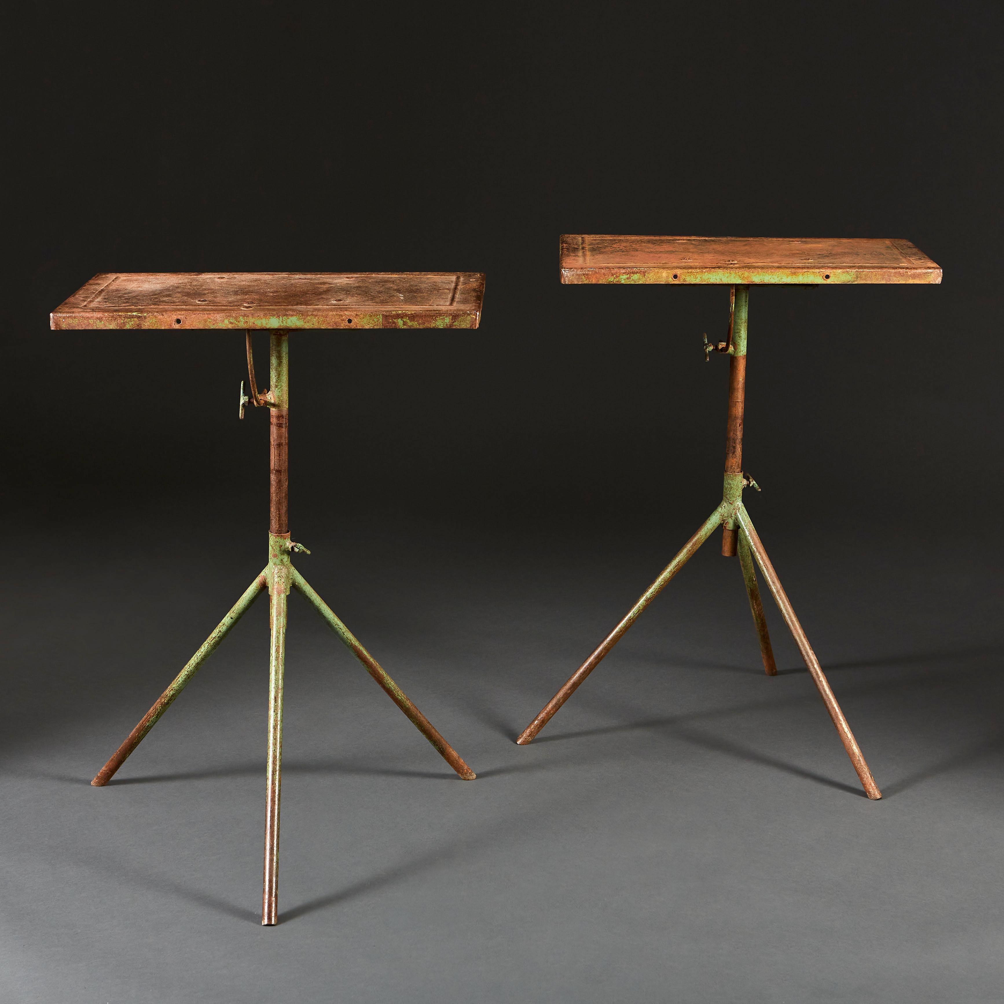 A pair of mid twentieth century industrial tables with green painted tripod bases, with adjustable stems to alter the height, and rectangular adjustable tilt tops. 

Measures: Height as photographed 80.50cm
Height at full extension 90.50cm.