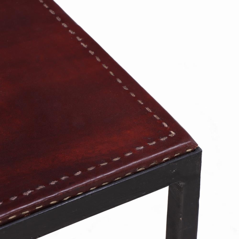 Una sofisticata coppia di tavolini artigianali ispirati all'eleganza minimalista di Jean-Michel Frank. Ogni tavolo presenta un'elegante struttura in ferro con una sottile patinatura e piani in pelle con cuciture a contrasto. Ideale come tavolino in