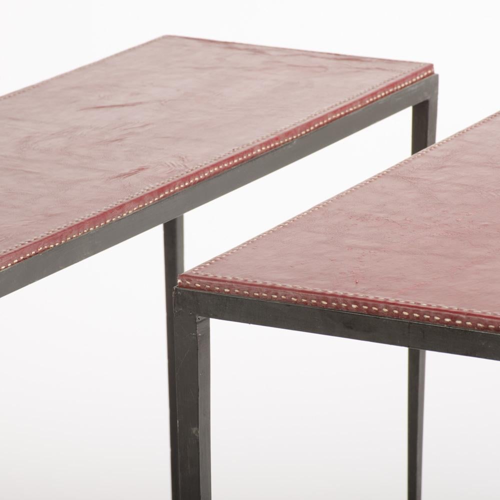 A pair of modern iron an hand-stitched dark burgundy leather console tables in the manner of Jean-Michel Frank.