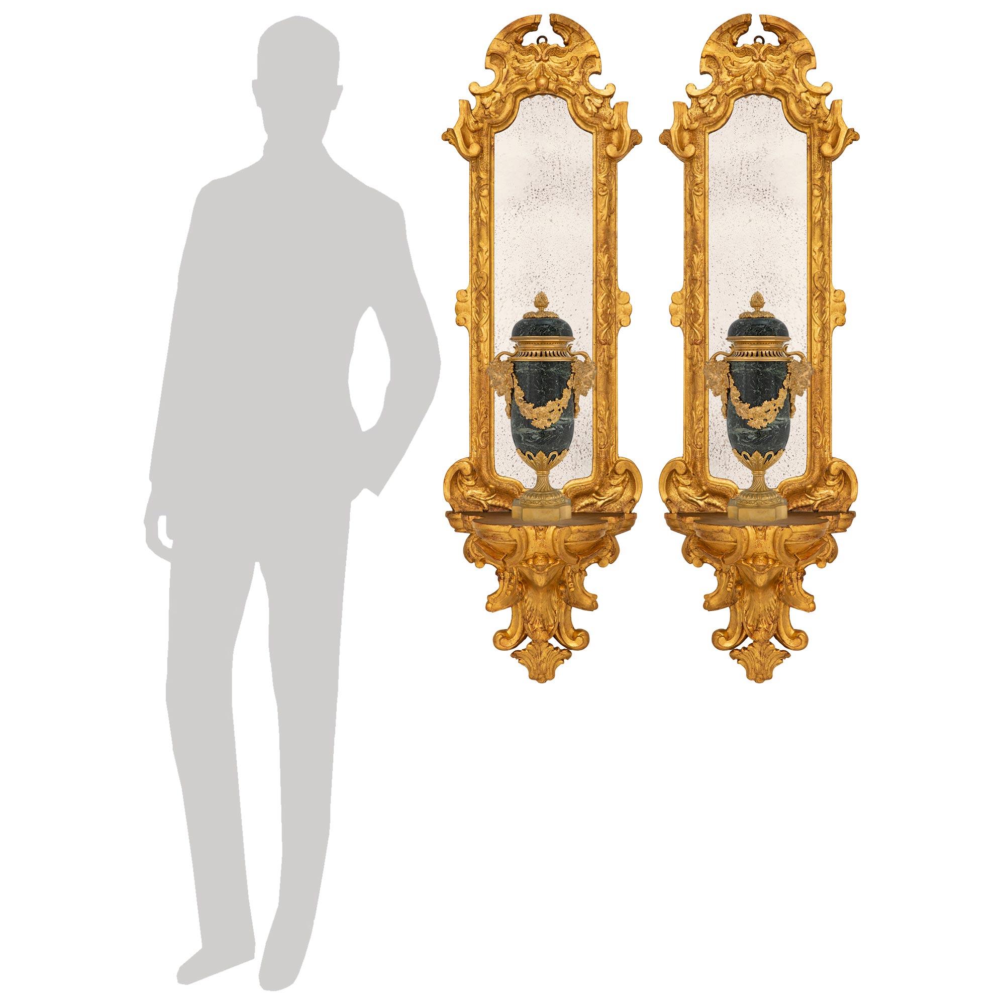Una splendida coppia di mensole da parete a specchio in legno dorato del periodo barocco italiano del XVII secolo, finemente dettagliate. Ogni staffa da parete è centrata da un'imponente mensola inferiore riccamente intagliata con eleganti disegni a