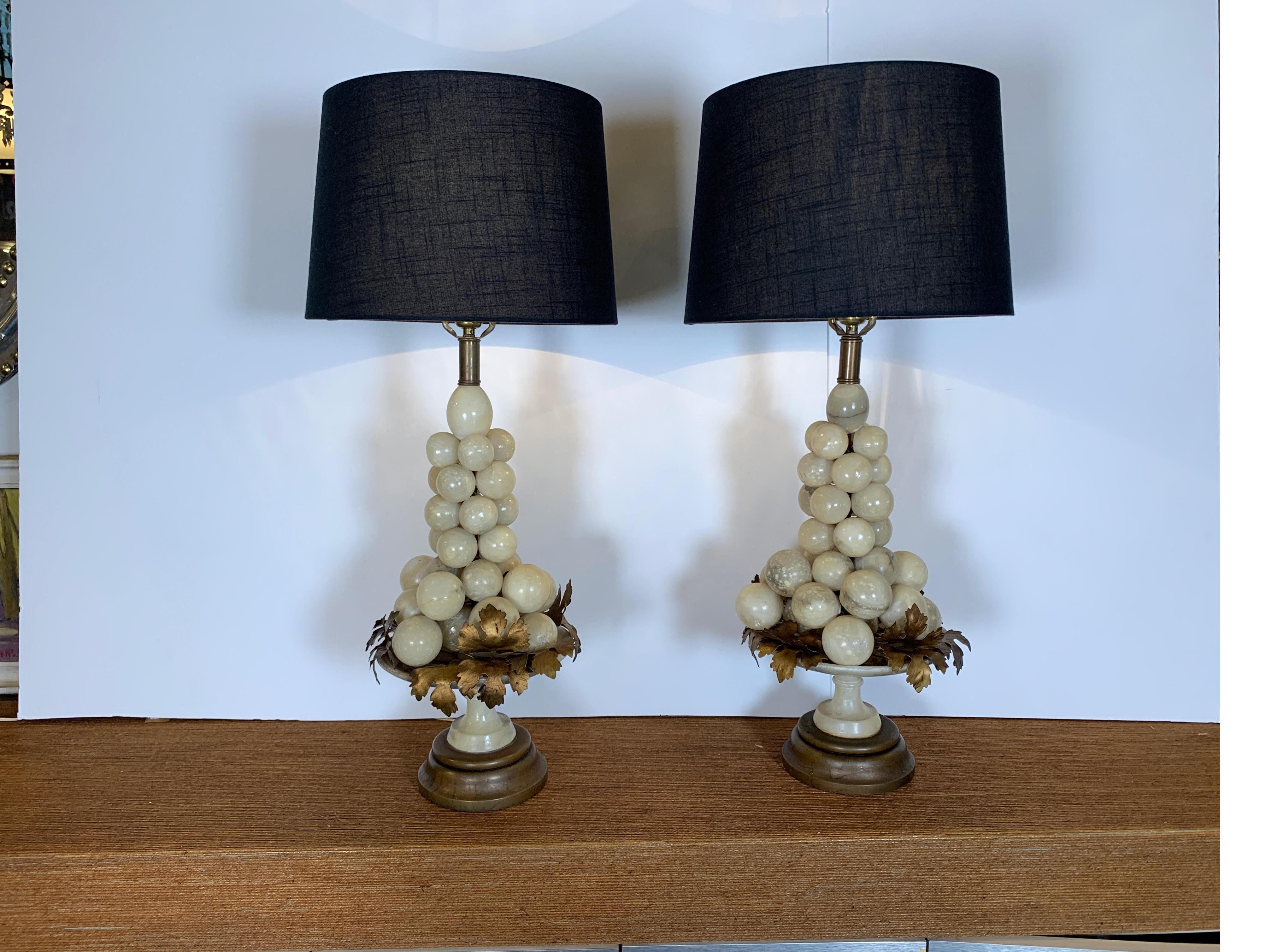 A whimsical and stylish pair of polished alabaster lamps. The lamps are a stacked grouping of stone grapes resting on gilt metal leaves with an alabaster compote style pedestal base on a wood bottom. Mid-20th century 26 inchest tall to the top of