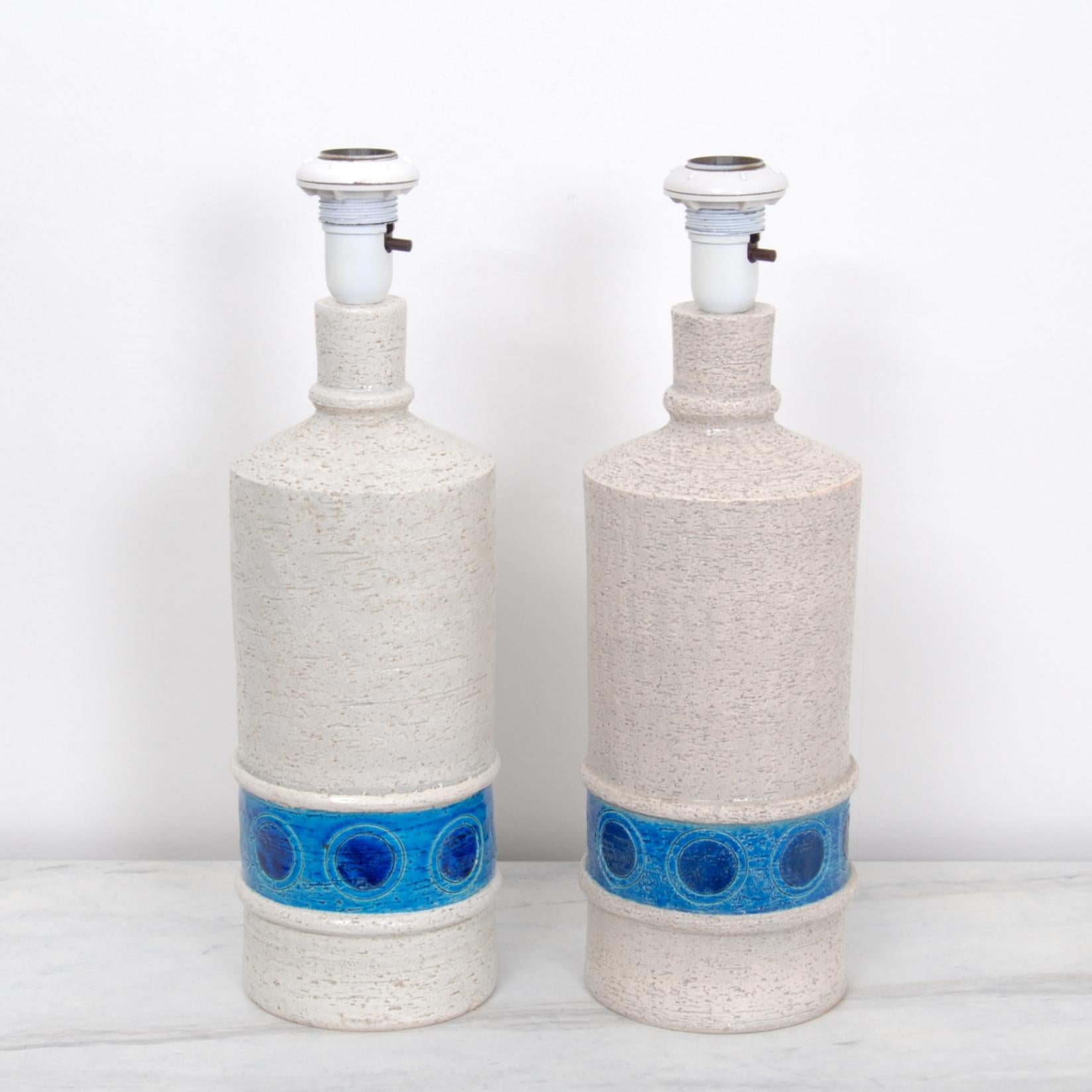 A pair of Bitossi textured bone white glazed cylinder lamps with a cerulean blue band. 100W max bulbs. We are selling these table lamps without the shades. Rewired.
  