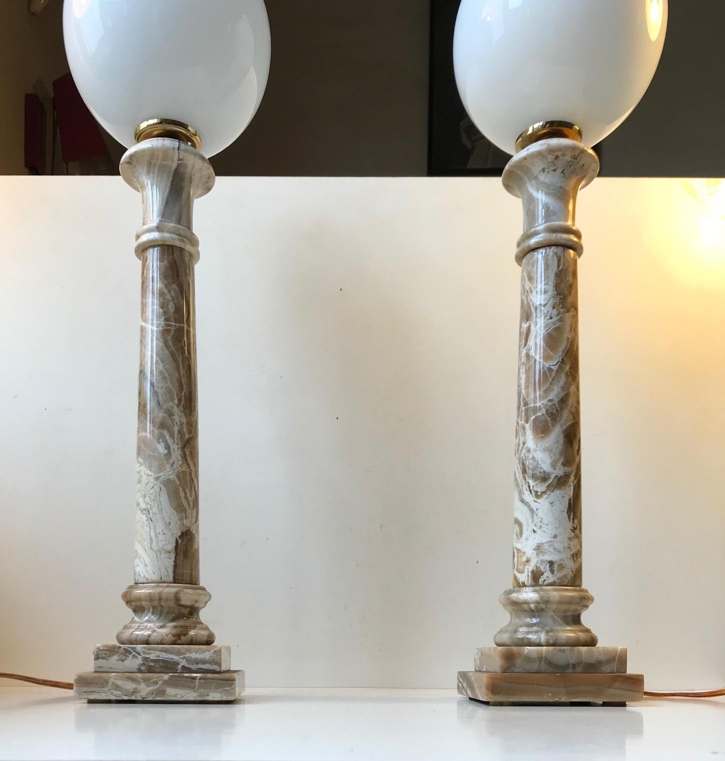 A pair of matching Art Deco revival onyx art table lamps. The shape resembles architectural columns. This type on onyx marble resembles Travetine. They are mounted with matching opaline glass spheres. These were made by hand in Italy during the