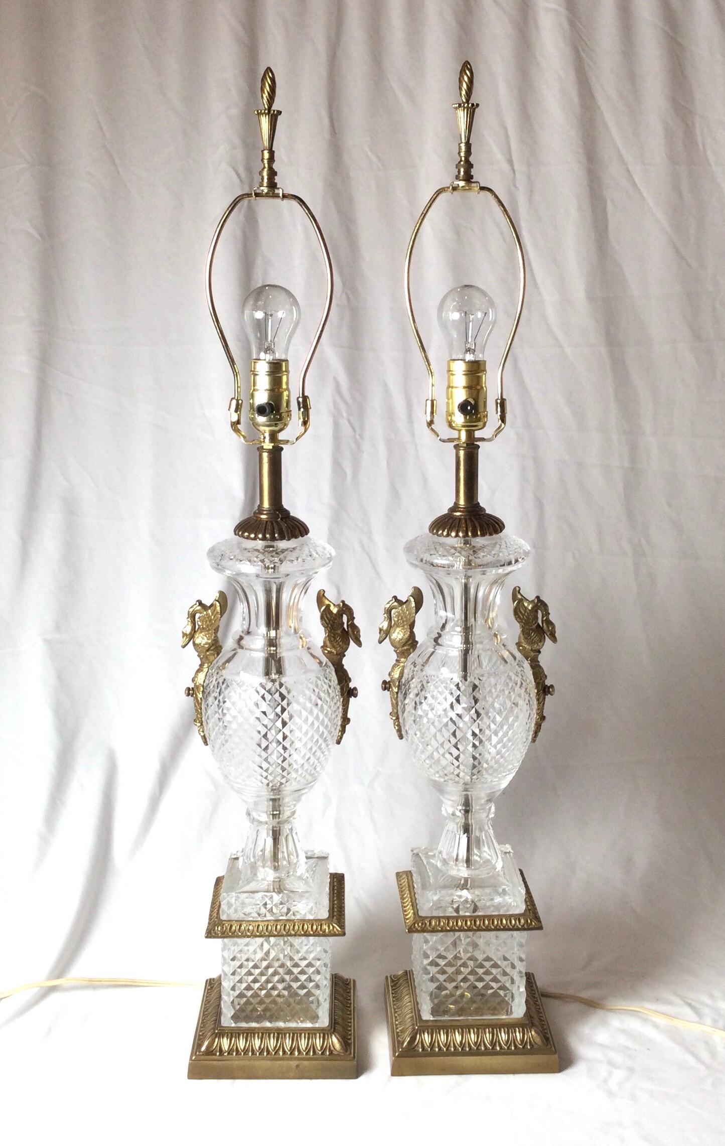 Elegant pair of diamond cut crystal neoclassical shaped lamps. The all-over diamond cut pattern with gilt cast brass mounts with swan motif. The shades are for photographic purposes only and not included with the lamps. 33 inches tall to the top of