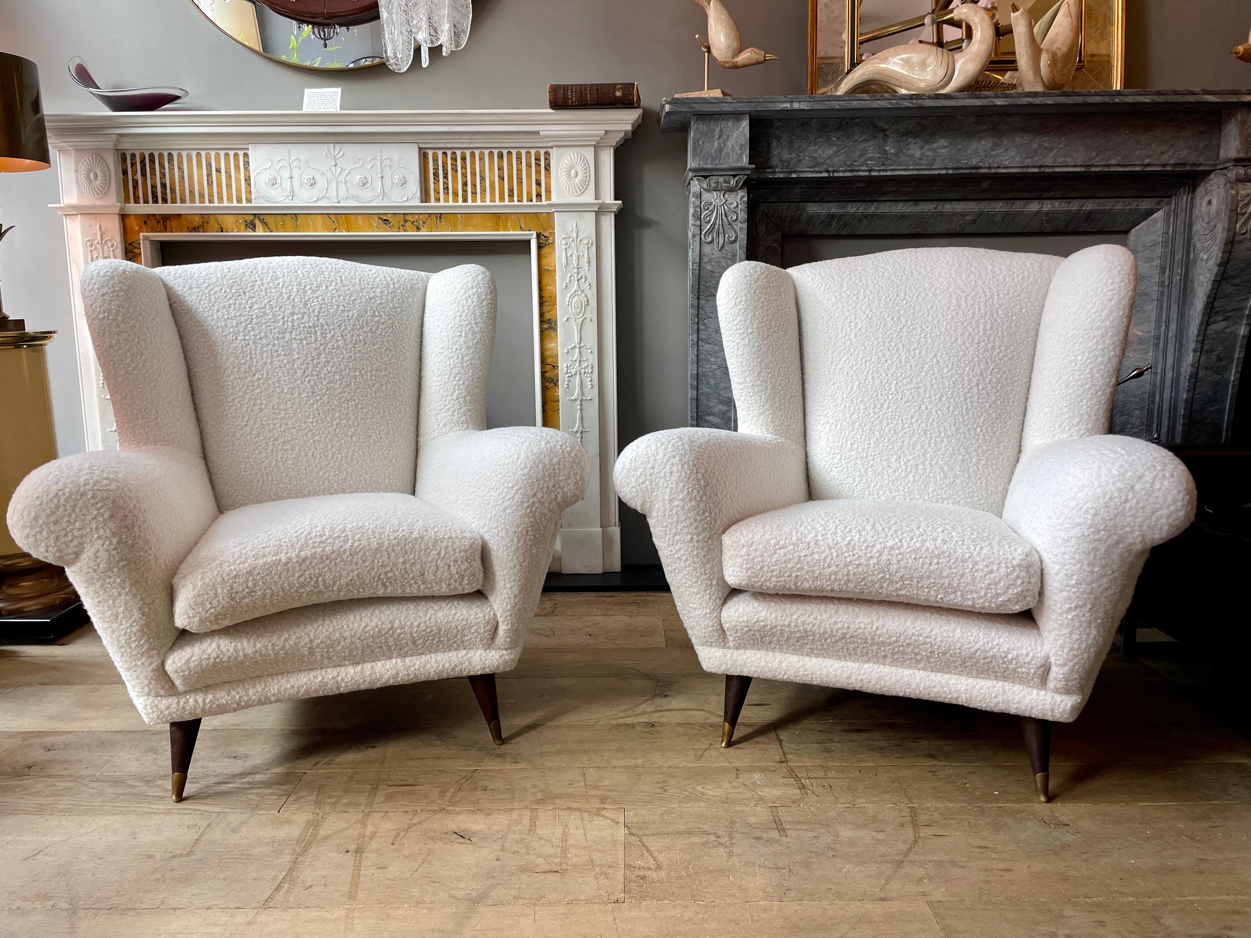 Une grande paire de fauteuils italiens à dossier ailé des années 1950, avec un design italien typique de l'époque, à la fois anguleux et courbé. Sur des pieds coniques en bois avec des pieds sabots en laiton. Le coussin de la chaise s'est formé et