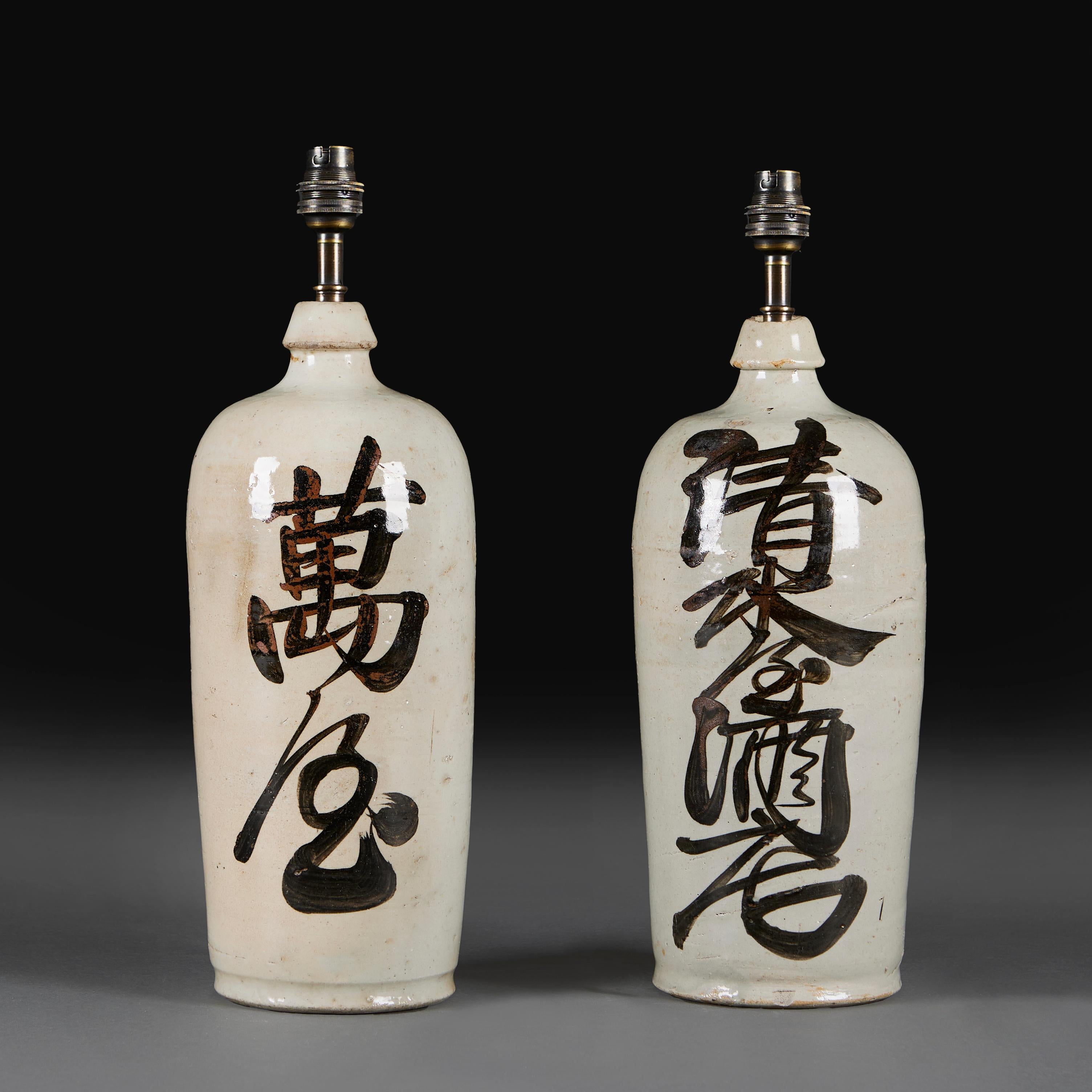 Un par de botellas de sake japonés de cerámica con escritura en tinta oscura, ahora montadas como lámparas.