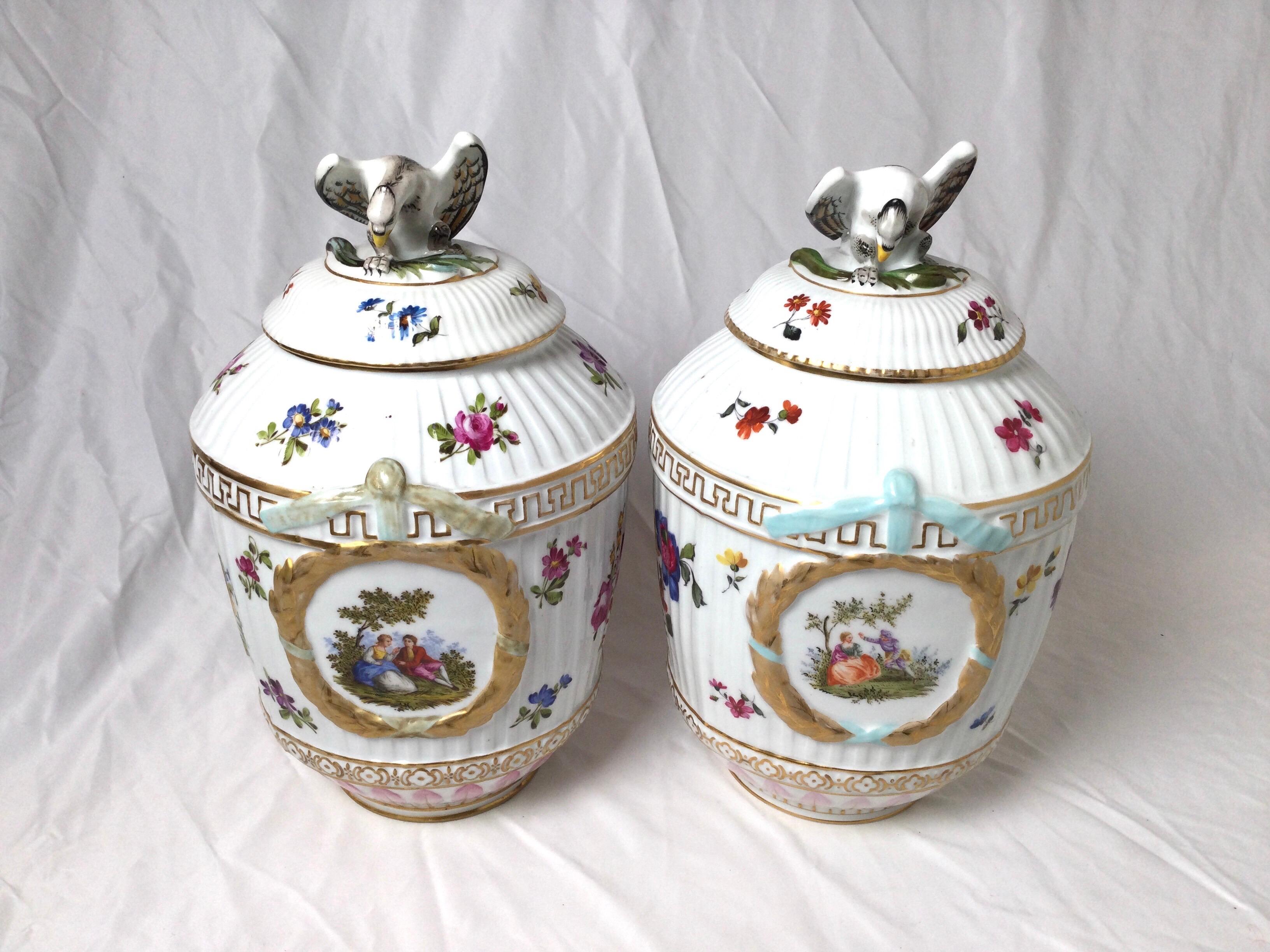 A pair of hand painted 19th Century KPM porcelain jars. The tops with eagle form finial sitting on a bulbous jar with ribbed surface hand painted with floral decoration with wreathed cartouches depicting courting couples. Blue underglaze mark on