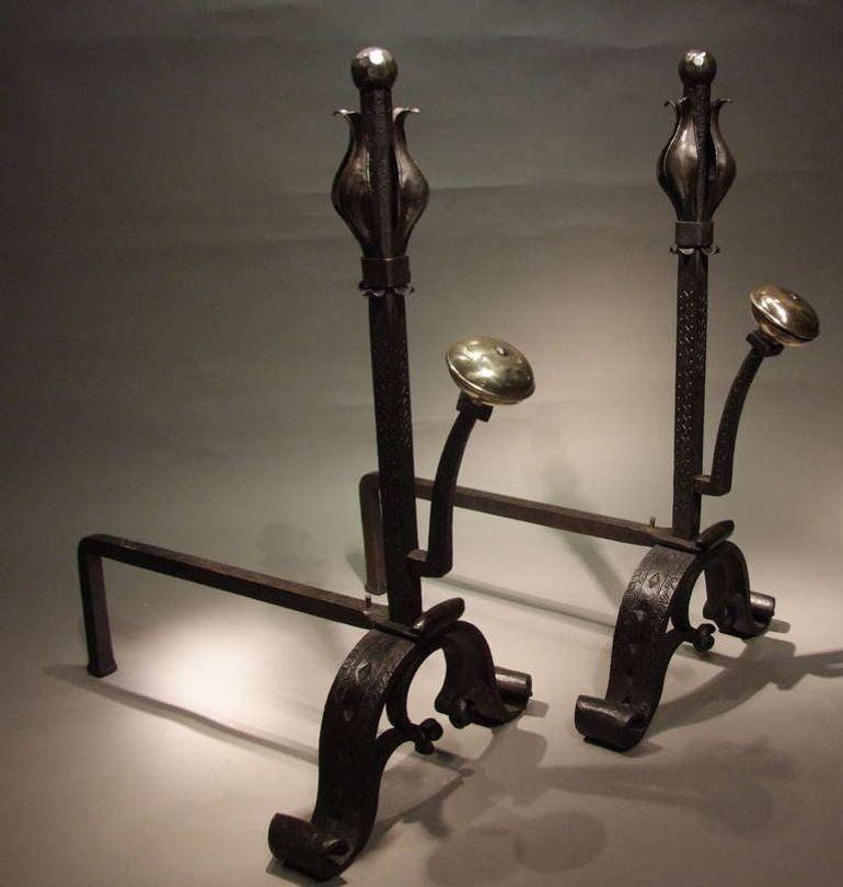 A pair of large and substantial Art and Crafts andirons in wrought iron with polished finials in the form of stylized tulips over etch decorated shafts having large spit supports with contrasting bronze suppressed ball finials.