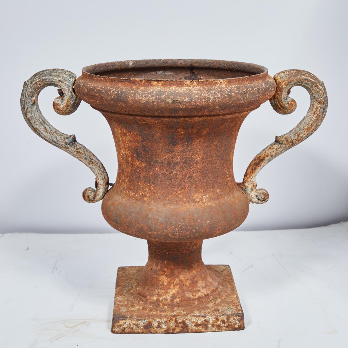 Pair of large 19th-century Italian iron urns with rounded rims, fluted, incurved bodies and scrolled handles. Resting on square pedestal bases, this elegant pair has a nicely weathered patina, and would enhance both indoor spaces and gardens alike.