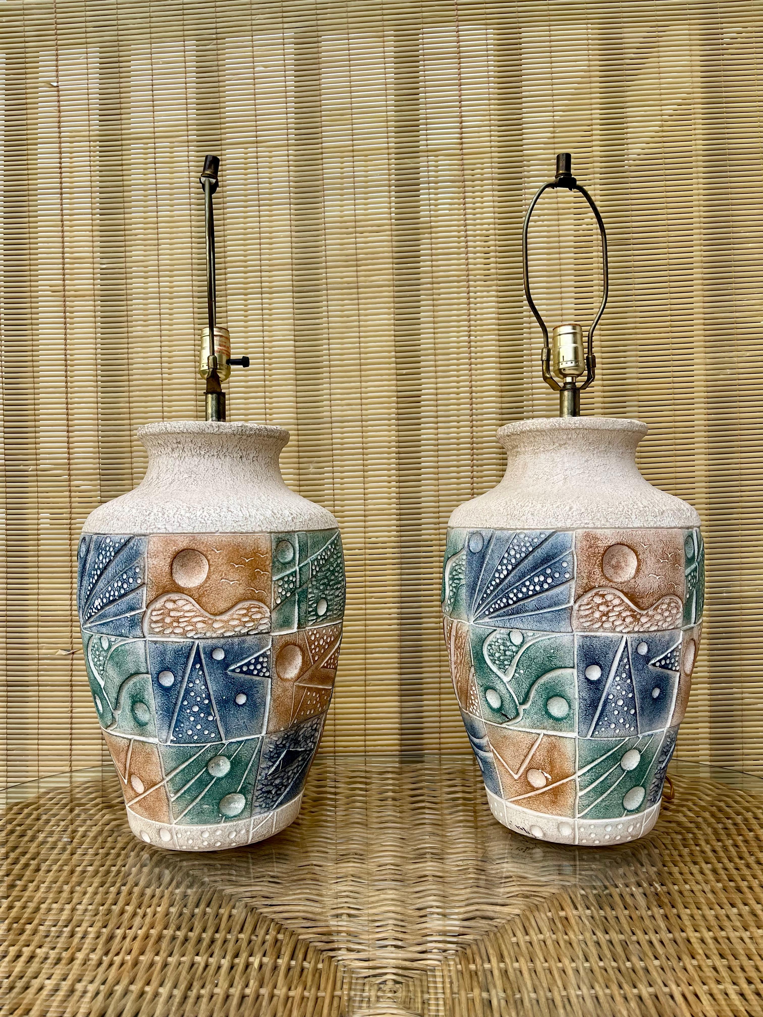 Paire de grandes lampes de table postmodernes en céramique de la fin du XXe siècle. 
Les grandes bases en céramique texturée présentent des détails géométriques abstraits gravés dans des tons sourds de bruns, de bleus et de verts. 
En bon état