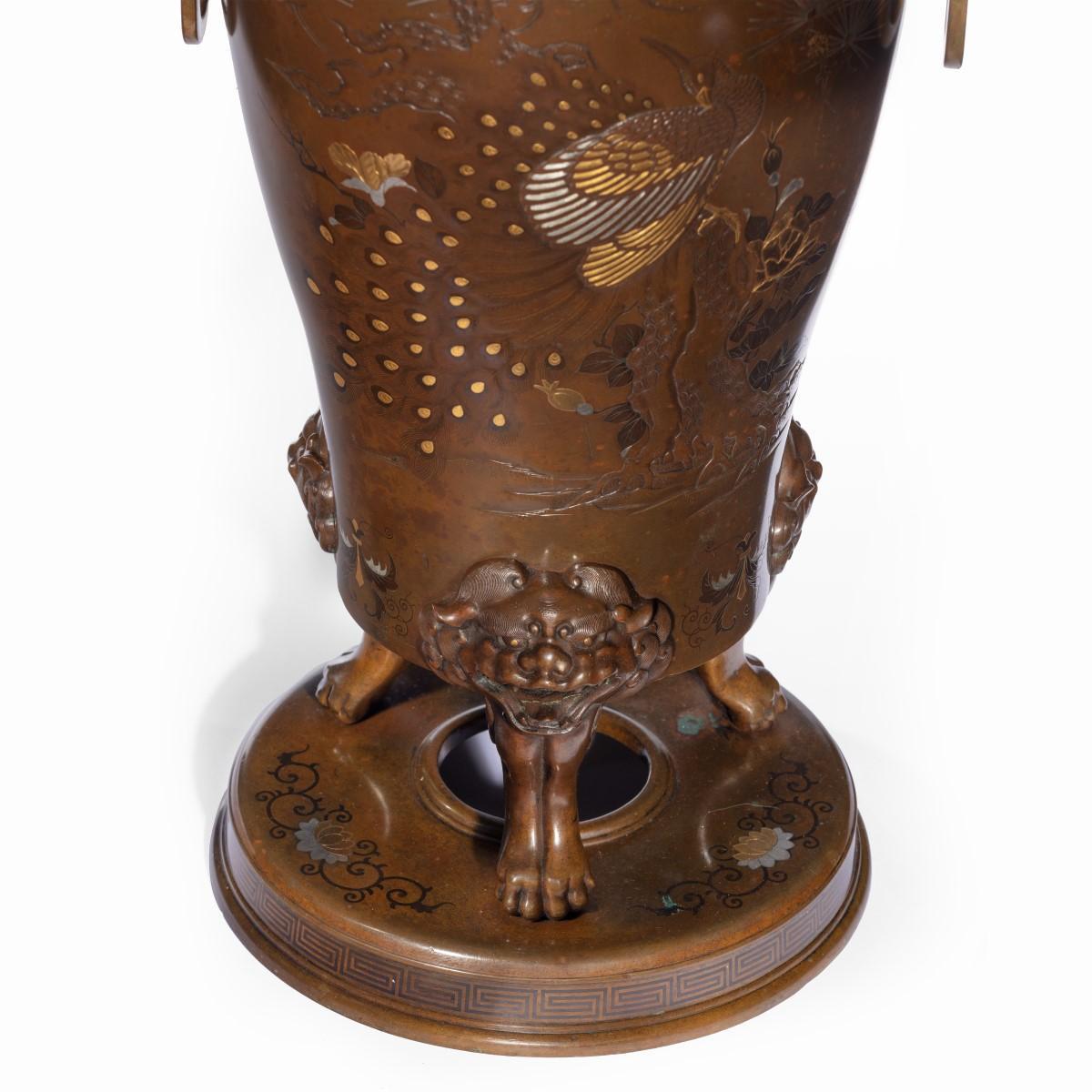 A pair of large Meiji period bronze vases, each of baluster form raised on three oni-mask feet on a ring-shaped base, applied with arched mask-and-ring handles, finely inlaid in patinated metals, silver and gilt with boys playing around a large