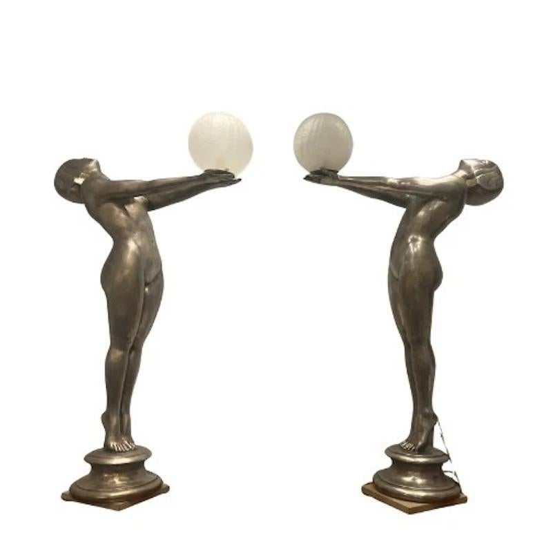 An extraordinary pair of large vintage lamps in the Art Deco Max Le Verrier style featuring sculptural nude female figures in a stylised pose, holding aloft frosted glass globes with crackle effect. 

These statement pieces exude all the glamour,