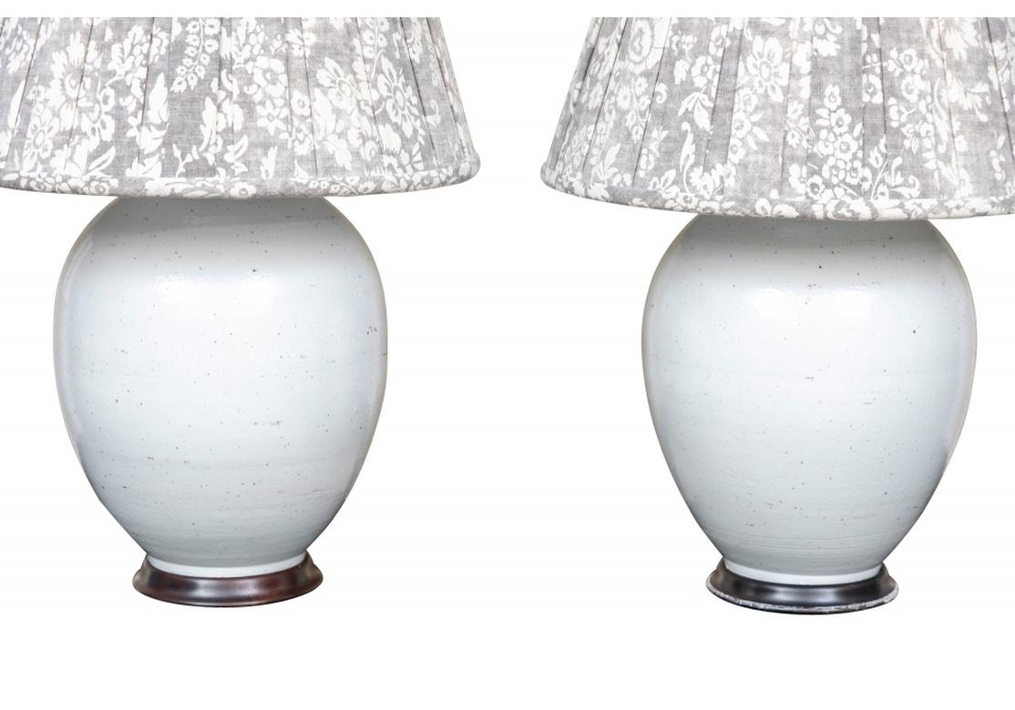 A fine pair of very large glazed pottery Jar Form Table Lamps mounted on turned wood bases. Large, ceramic, egg shaped table lamps have a white ground with a subtle black speckle. Quality Leviton brass sockets and fittings for two bulbs and height