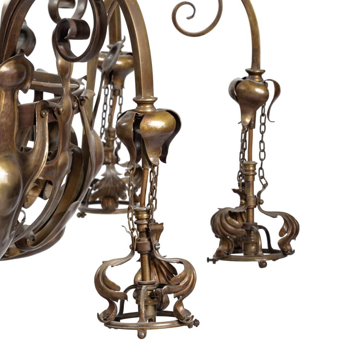 A pair of large Victorian 8-light brass chandeliers, each with a central rod with an acanthus leaf finial supporting eight C-scrolls attached to a central ring which, in turn, supports eight square section arms and pendent stylized floral sockets