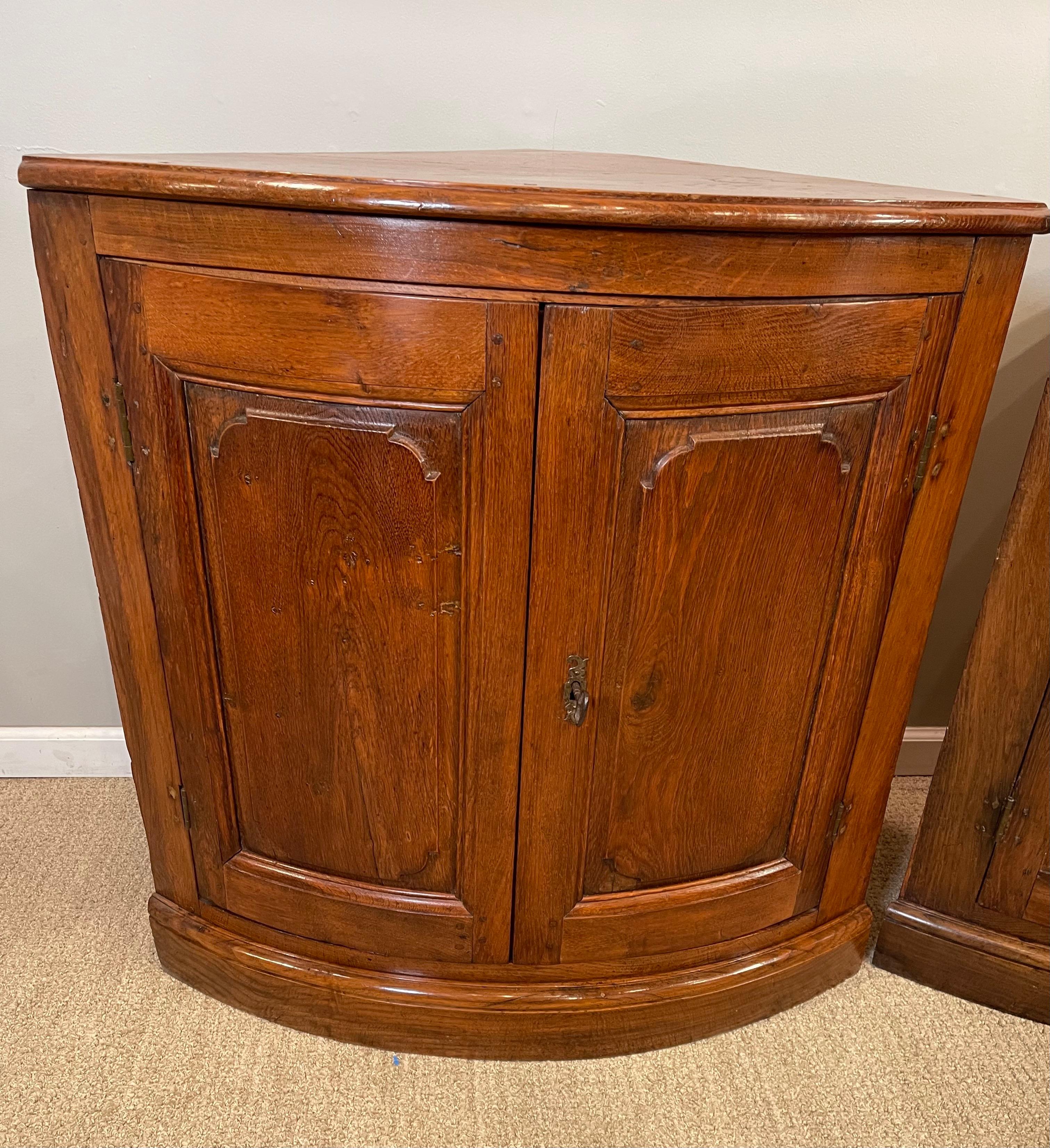 A Pair of late 17th century oak corner cabinets 
Each with an interior shelf. Left door latches with a locking right door. Doors with with raised beveled panels. Each cabinet retaining it’s original lock and key.
