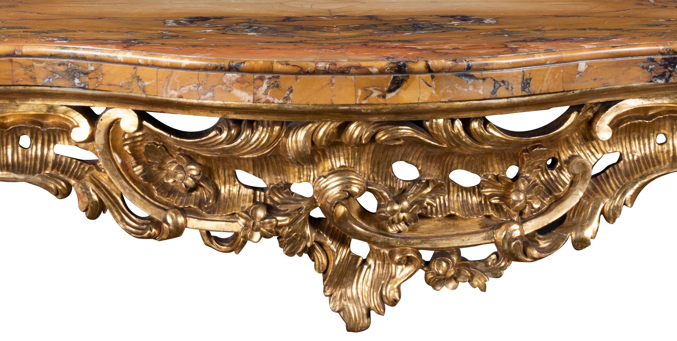 The serpentine fronted marble top with ovolo molded edge over carved rosettes, C scrolls and rocailles, the sides with conforming decoration, each canted cabriole leg headed with foliate scroll to leaf sabot and scroll foot, joined by x- form