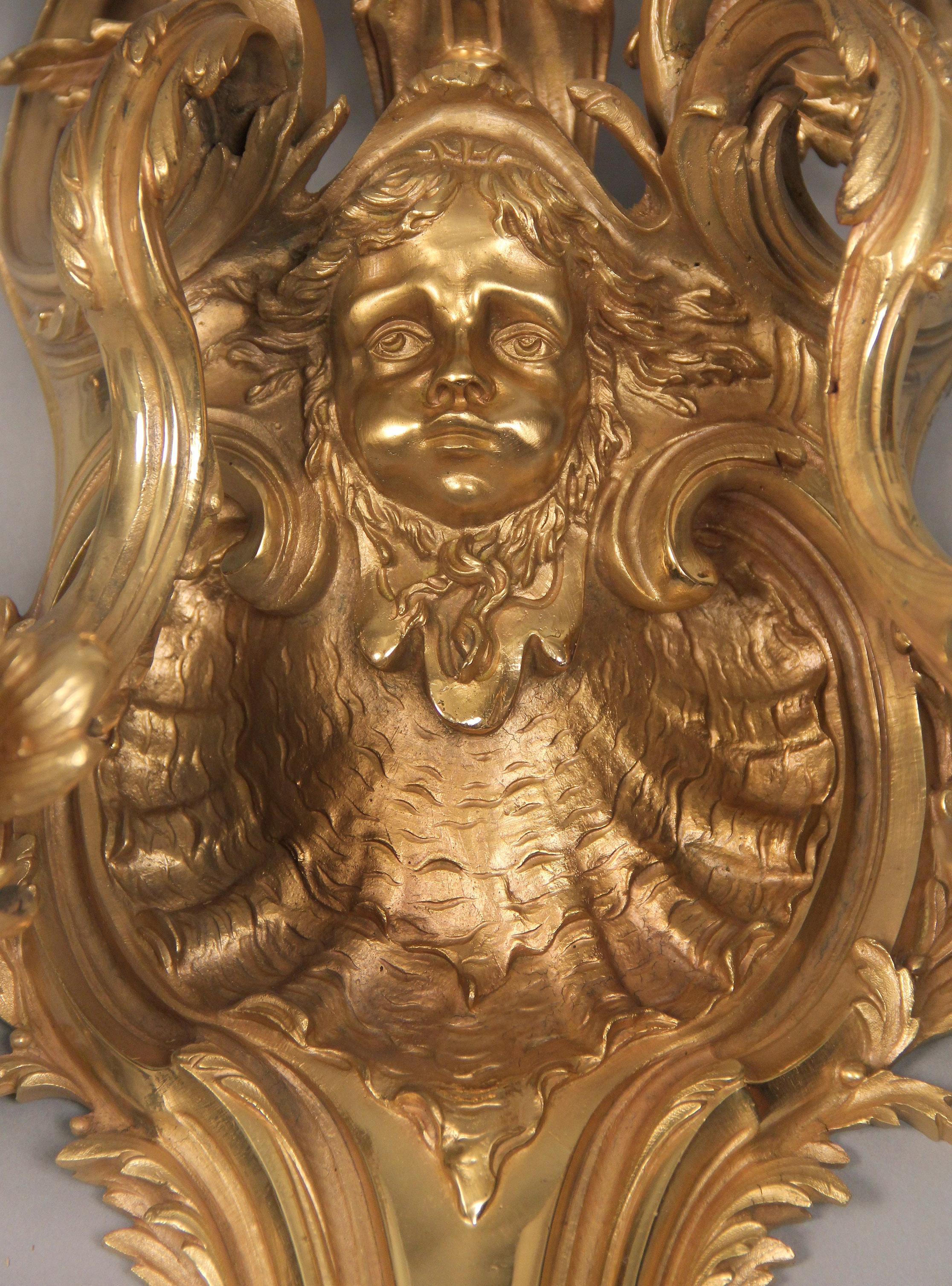 A pair of late 19th-early 20th century gilt bronze five-light sconces

Each backplate decorated with large cherub mask above a sea shell with five tiered lights.