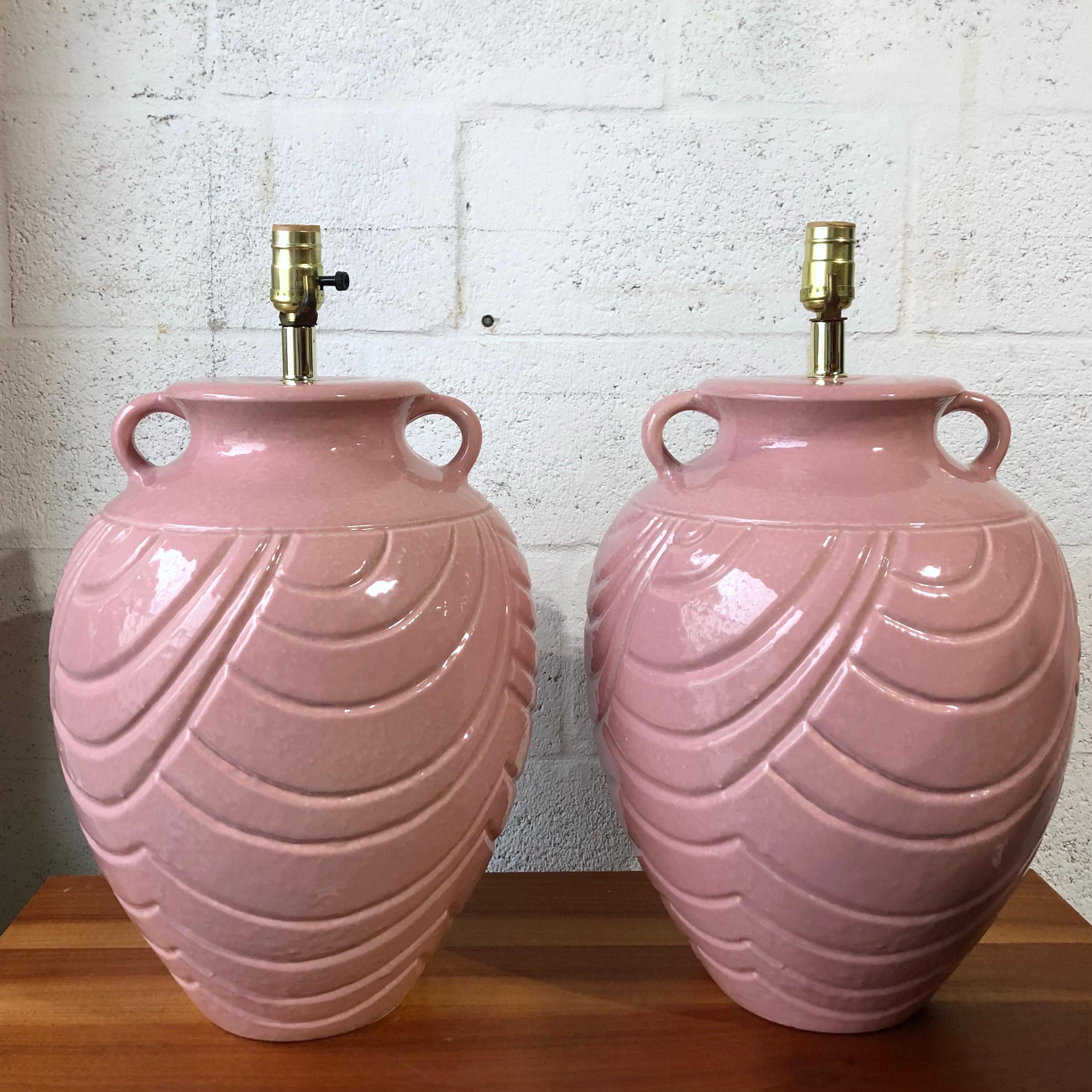 A pair of large late 20th century two handles jar ceramic table lamps. C 1980s
Feature a modernist interpretation of a traditional two handles water jar. With carved arches and a glossy soft pink ceramic glaze. 
The Lamps are in a very good